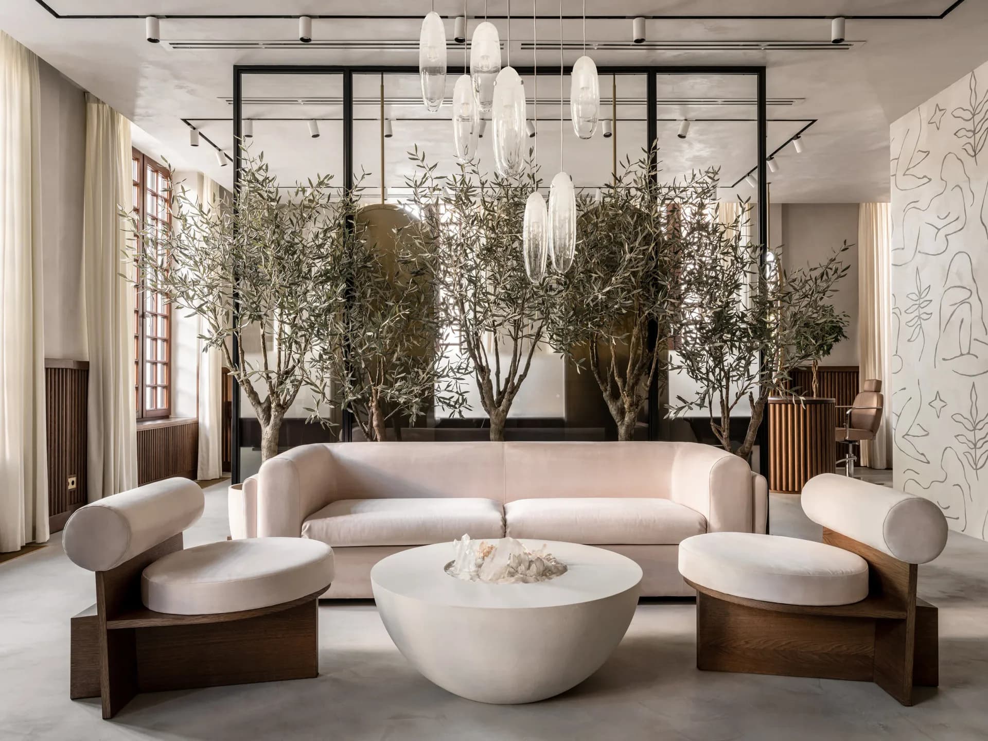 Luxurious living room with curved cream sectional sofa, sculptural white pendant lights, potted olive trees, and minimalist furniture by Julien Albertini.