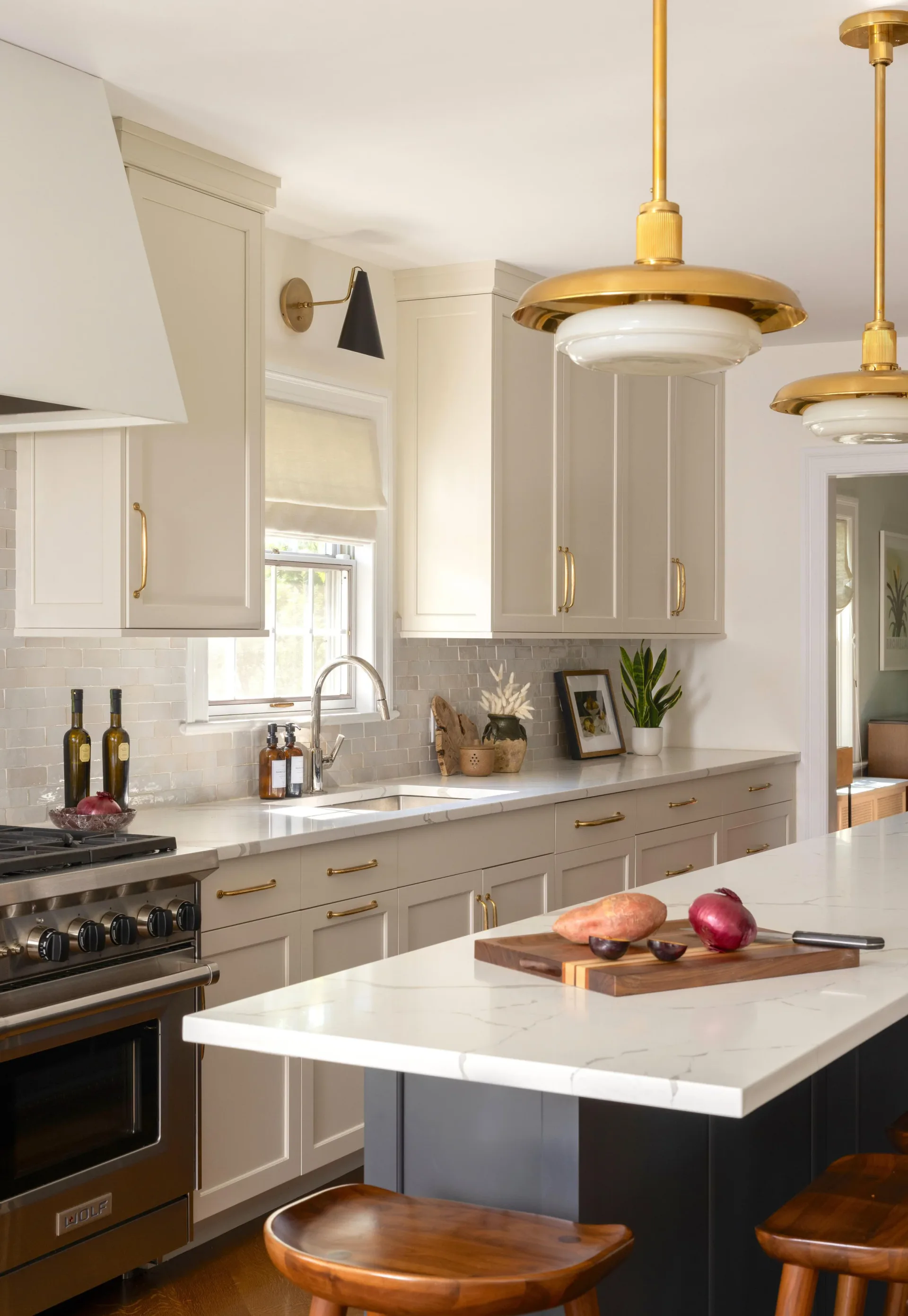 Modern kitchen featuring taupe cabinetry, white marble countertops, brass pendant lighting, and a black island with wood seating by Julieta Alvarez.