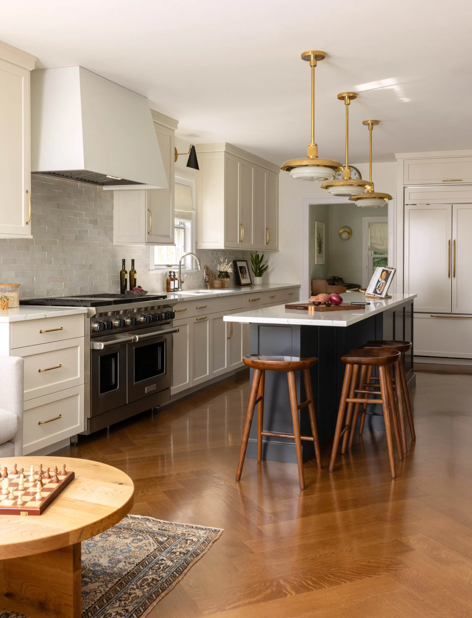 Modern kitchen with cream cabinetry, black range, black island with wood barstools, brass pendant lights, and white subway tile backsplash by Julieta Alvarez.