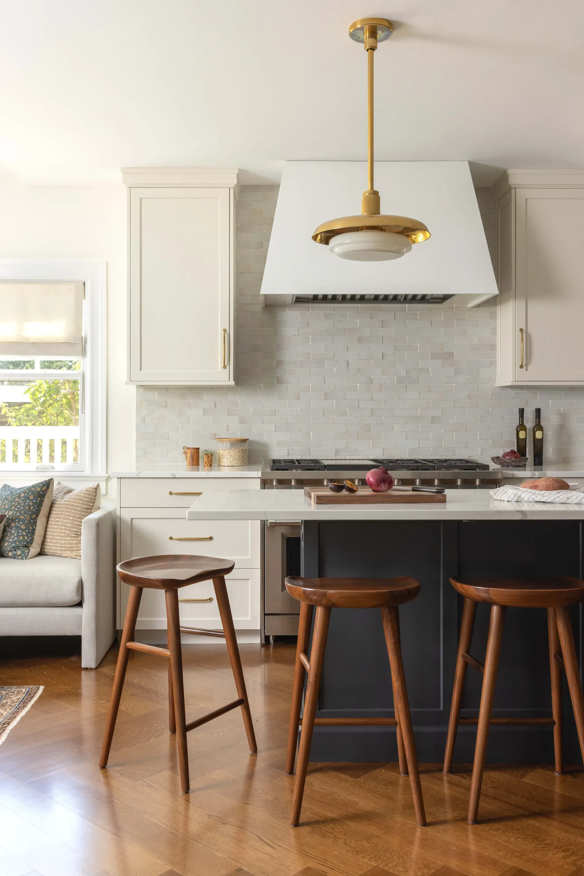 Modern kitchen with white cabinetry, marble backsplash, black island with wooden bar stools, and brass pendant lighting by Julieta Alvarez.
