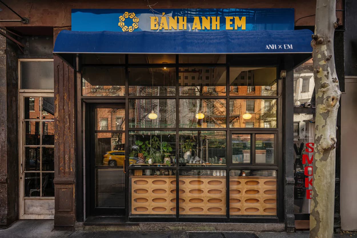 Banh Anh Em storefront with blue signage, wooden display windows, and warm interior lighting designed by Junho Choi.