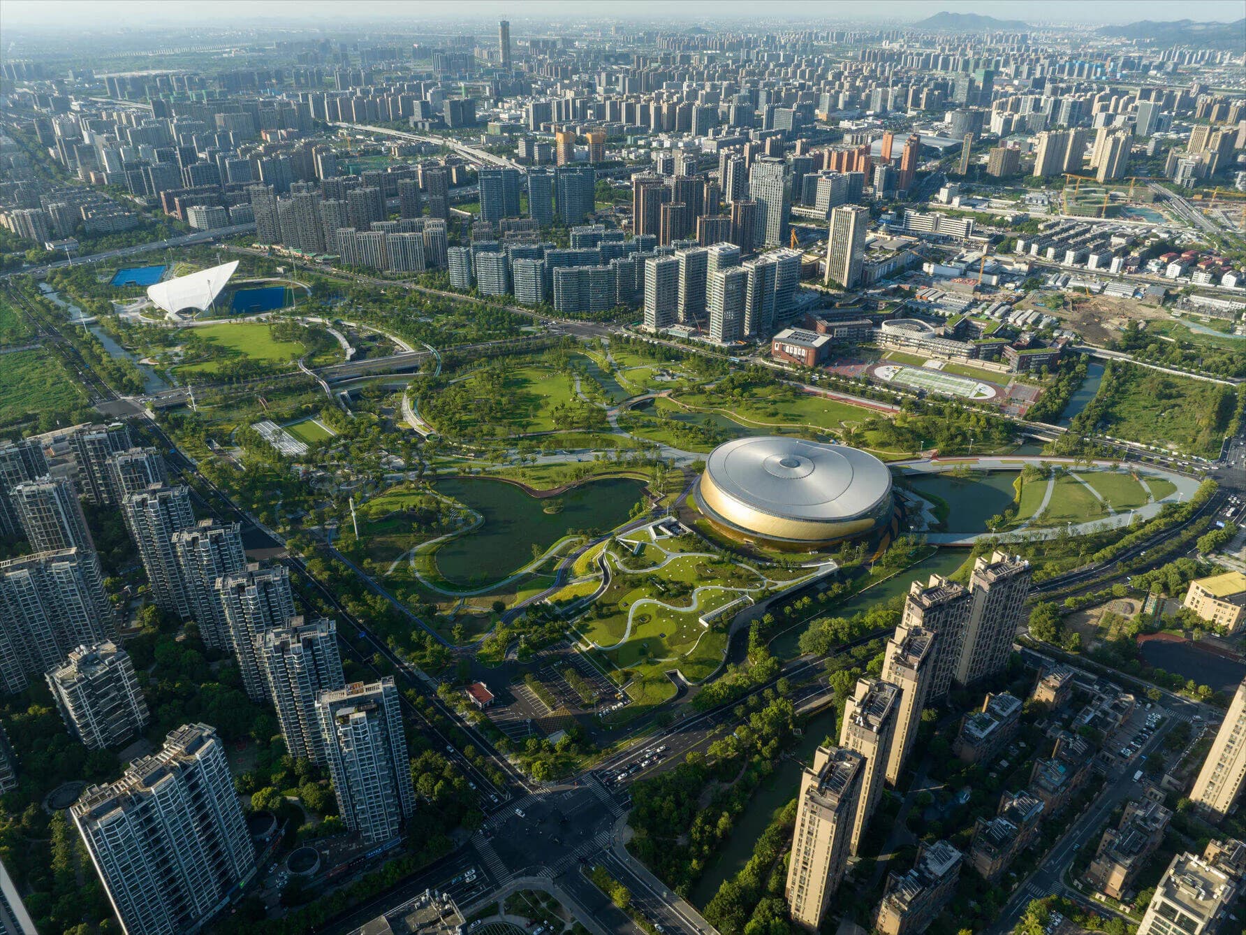 Aerial view of a large modern circular building with curved pathways and extensive green landscaping surrounded by dense urban development by Justin Korhammer.
