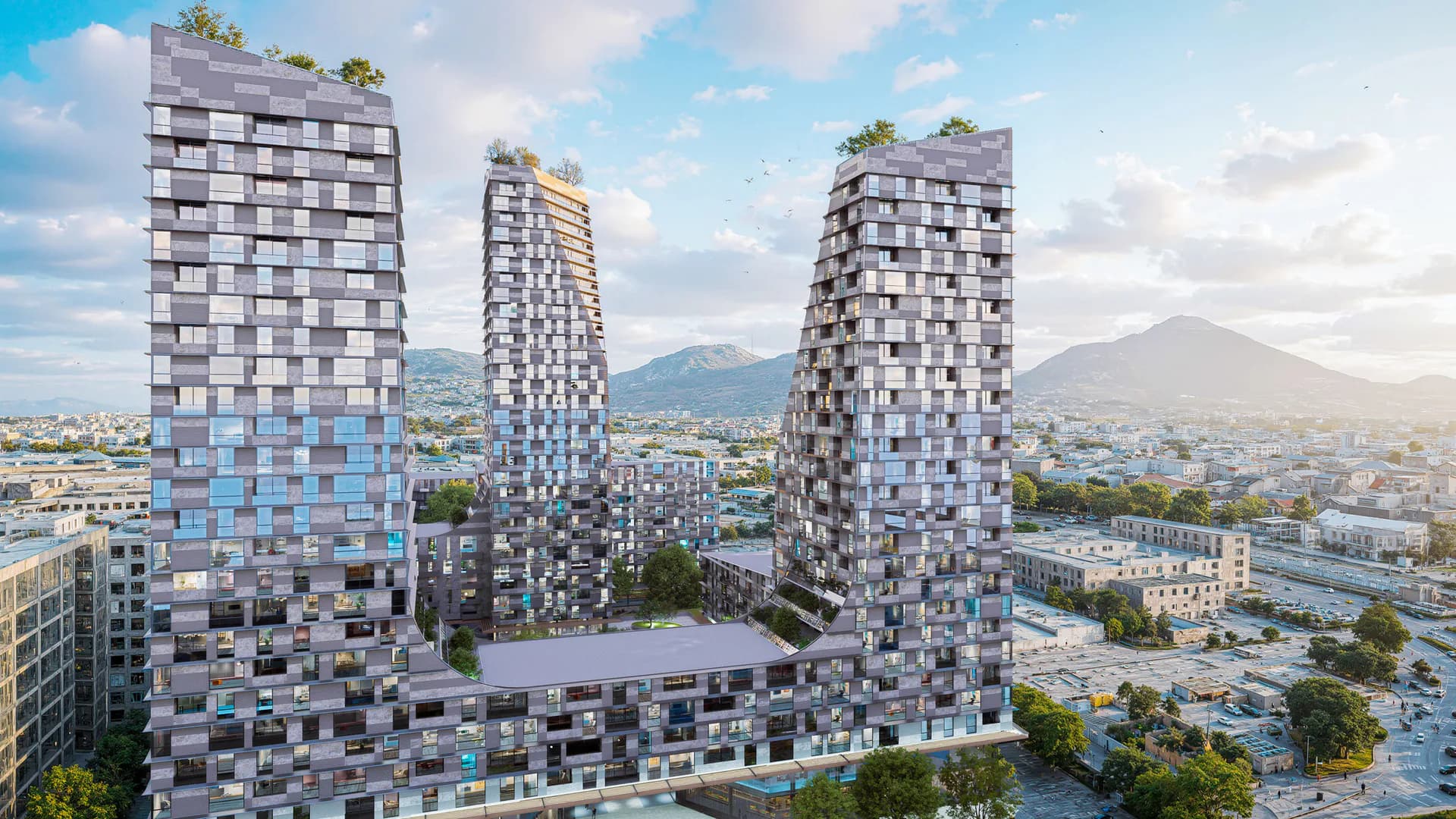 Three residential towers with staggered blue and gray facades rise against mountains and sky in this architectural rendering by Justin Korhammer.