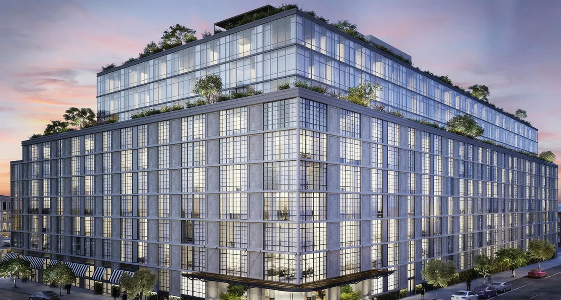 Modern multi-story commercial building with extensive glazing, steel framework, and rooftop greenery against twilight sky, designed by Jutta Ishii.