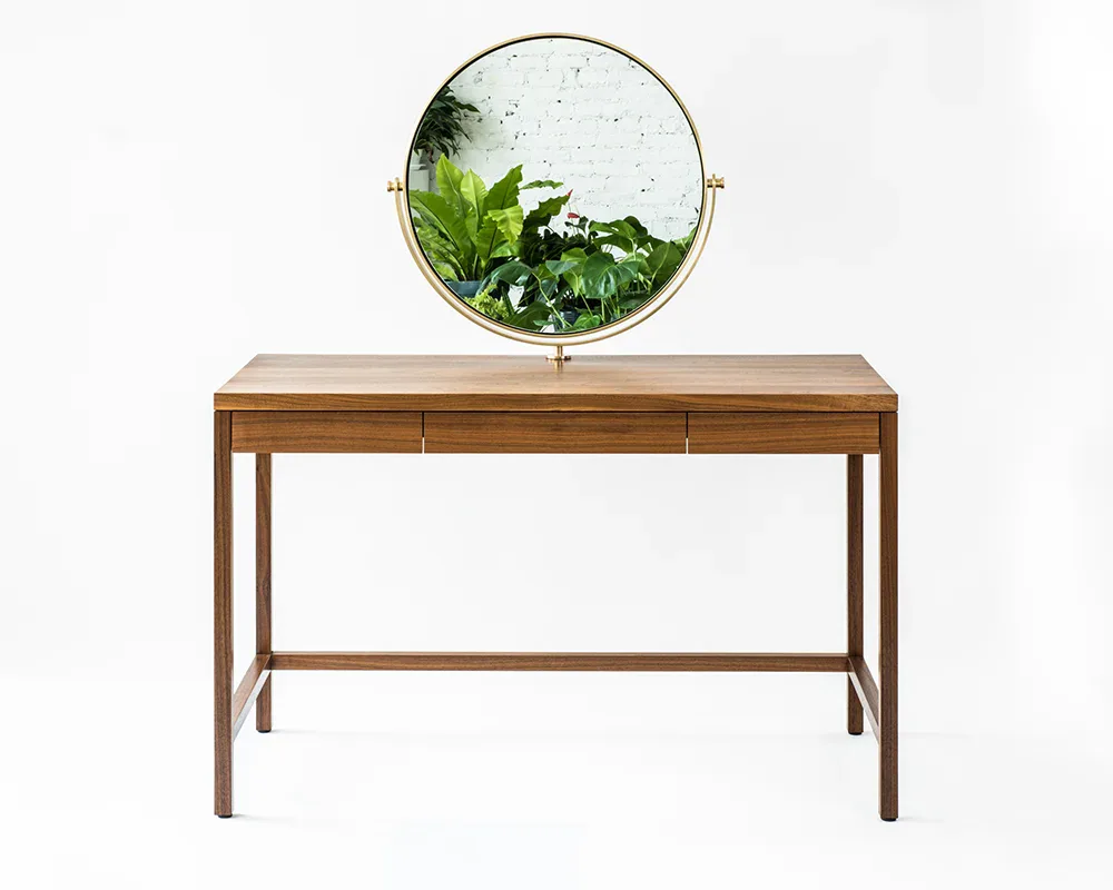 Mid-century modern wooden desk with three drawers and brass circular mirror mounted above, styled with potted plants, by Kai-wei Hsu.