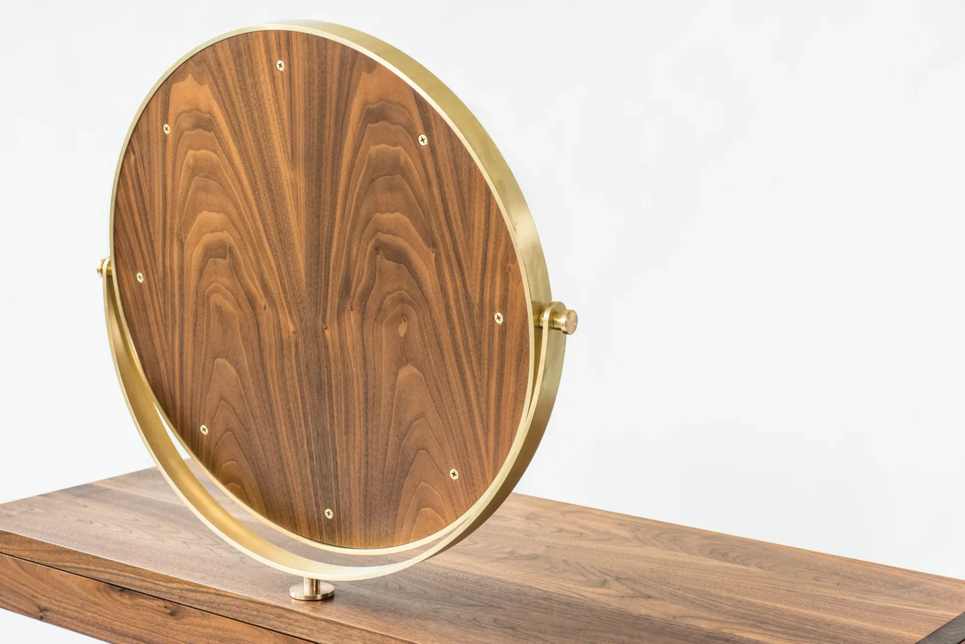 Oval wooden mirror with walnut veneer and brass frame mounted on a wooden base, showcasing minimalist furniture design by Kai-wei Hsu.