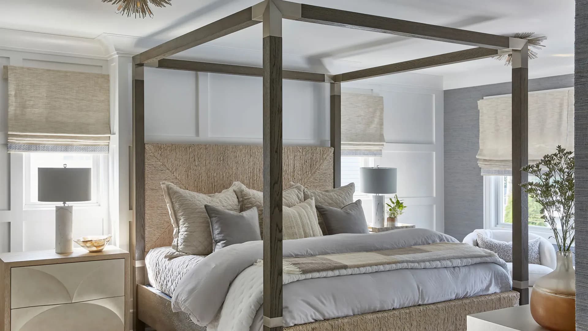 Modern canopy bed with dark wood frame, upholstered seagrass headboard, neutral linens, and layered bedding in a bright bedroom with large windows by Karen Wolf.