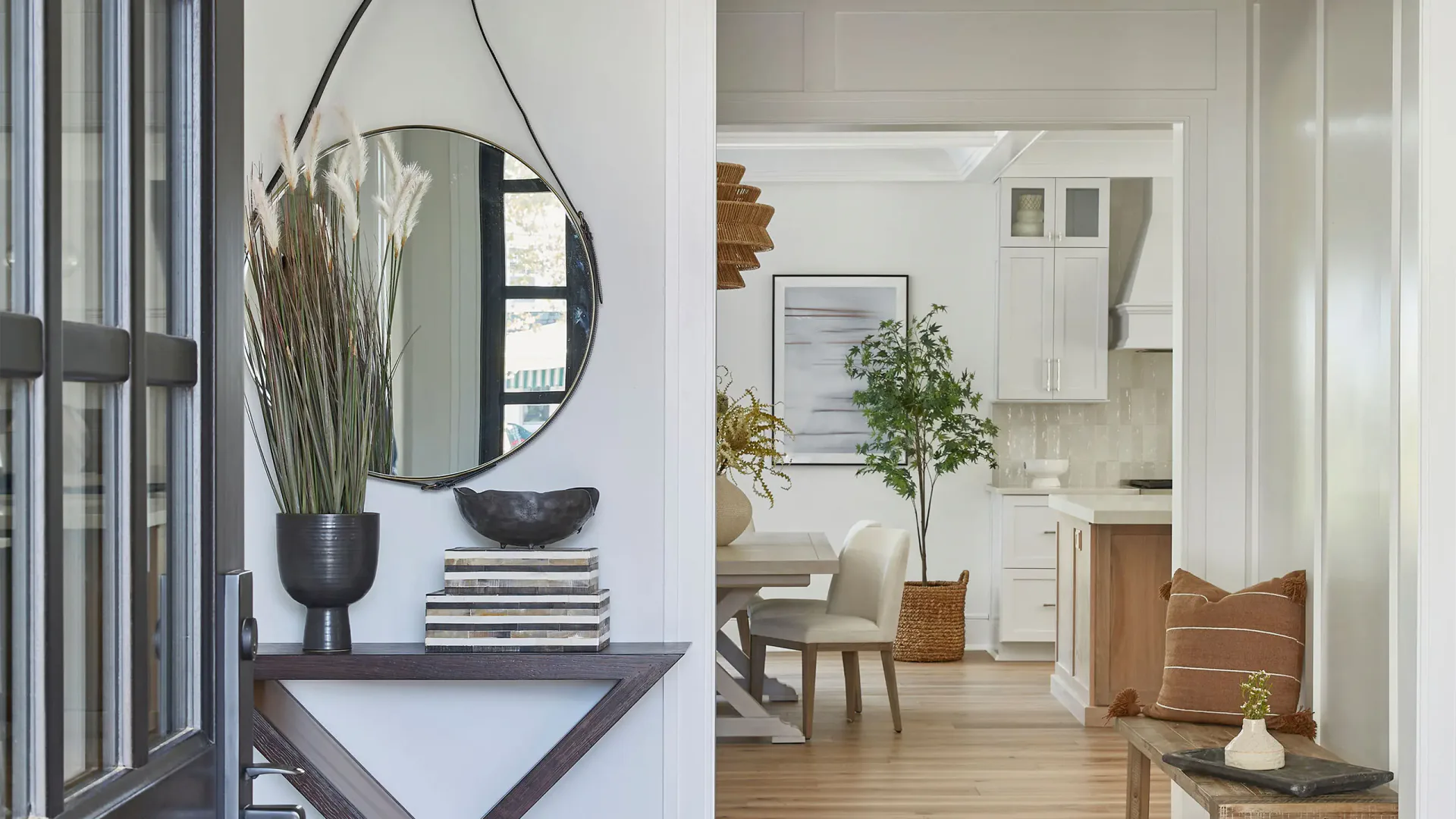 Modern entryway and living space featuring a round mirror, potted plants, wooden flooring, and minimalist furnishings in neutral tones by Karen Wolf.