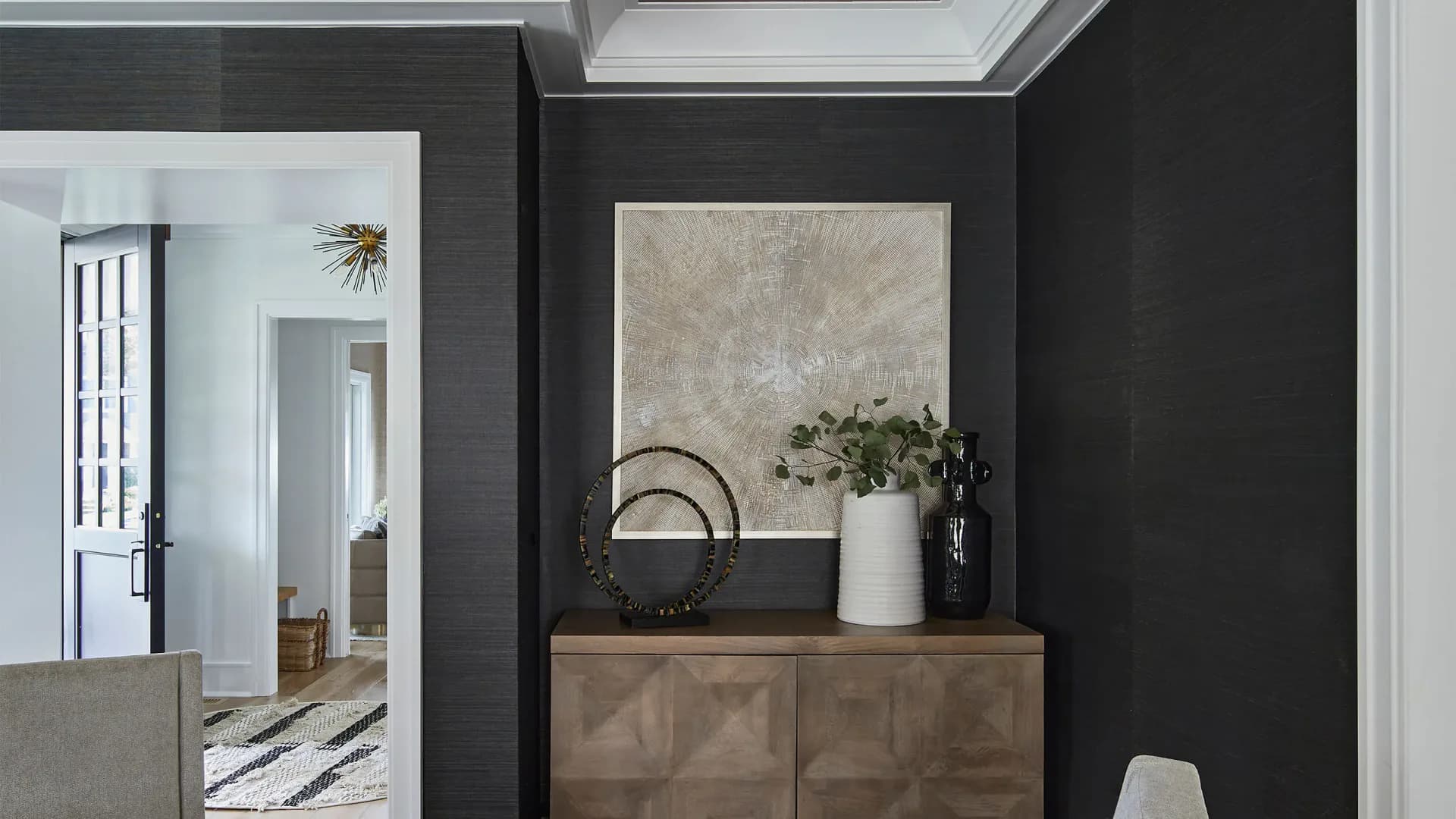 Modern entryway with charcoal walls, wooden dresser with decorative objects and mirror, and white ceiling detail by Karen Wolf.