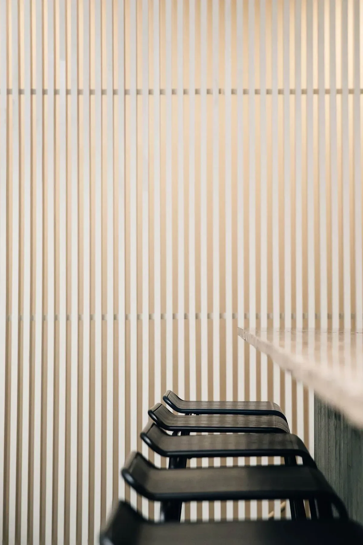 Minimalist interior with black lounge chairs against a cream corrugated wall with horizontal shadow patterns by Kari Minami.