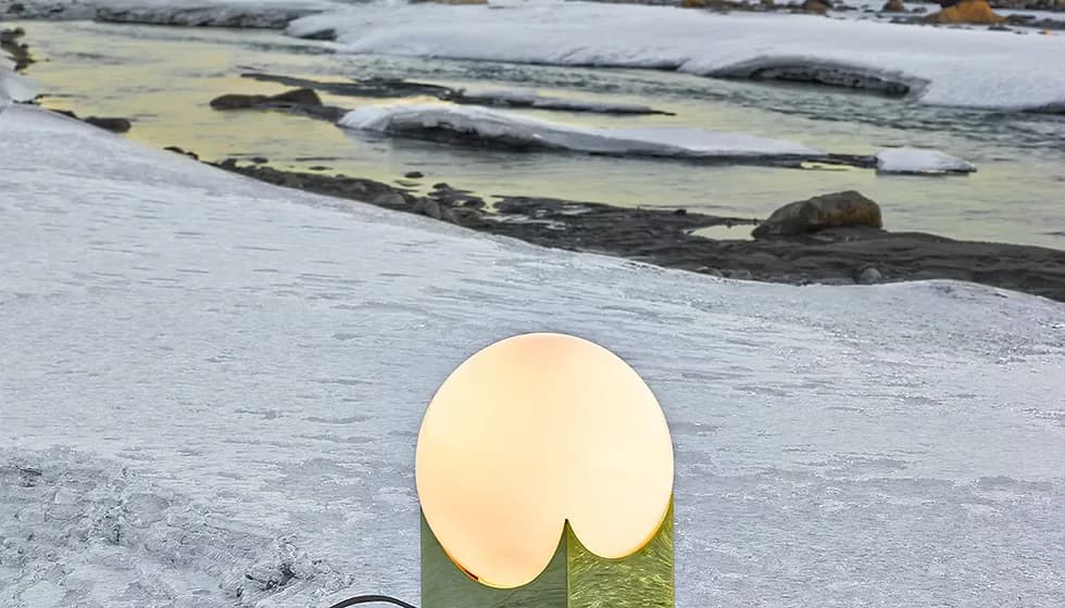 Minimalist lighting design featuring a warm cream-colored spherical lamp mounted on a green geometric base overlooking a rocky coastline, by Karl Zahn.