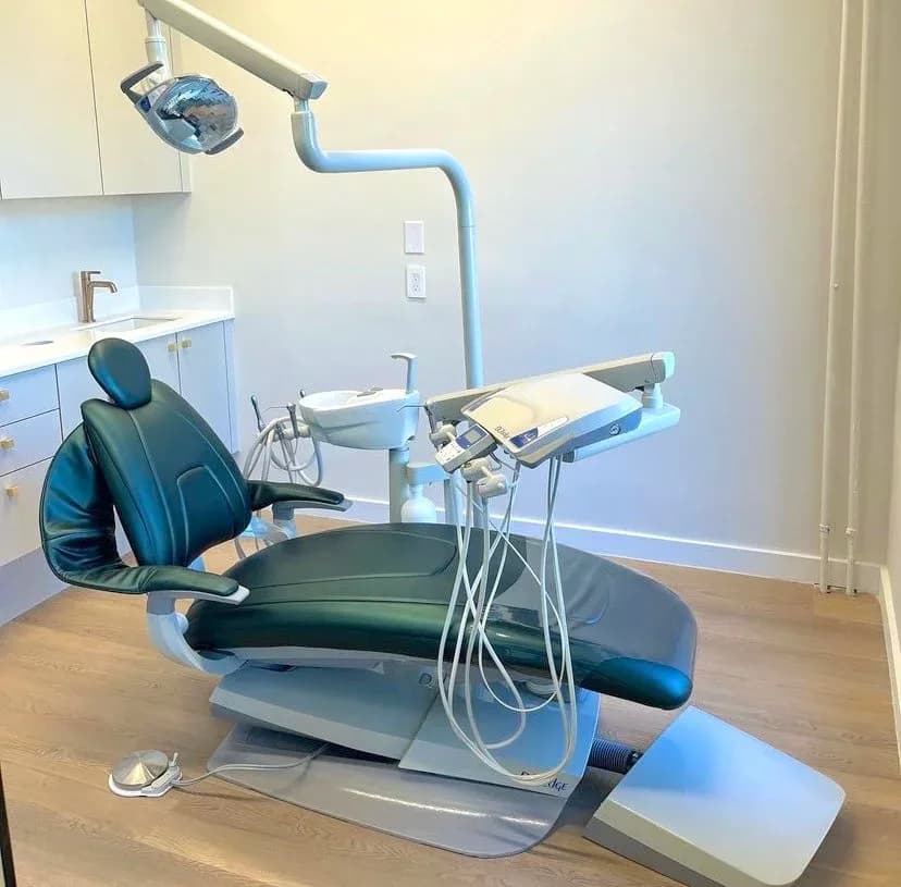 Modern dental operatory with blue upholstered chair, overhead surgical light, and white cabinetry, designed by Karla Quiroz.