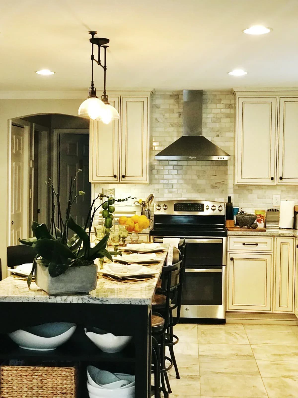 Cream kitchen with black island, stainless steel range hood, subway tile backsplash, and pendant lighting designed by Katherine Flores.