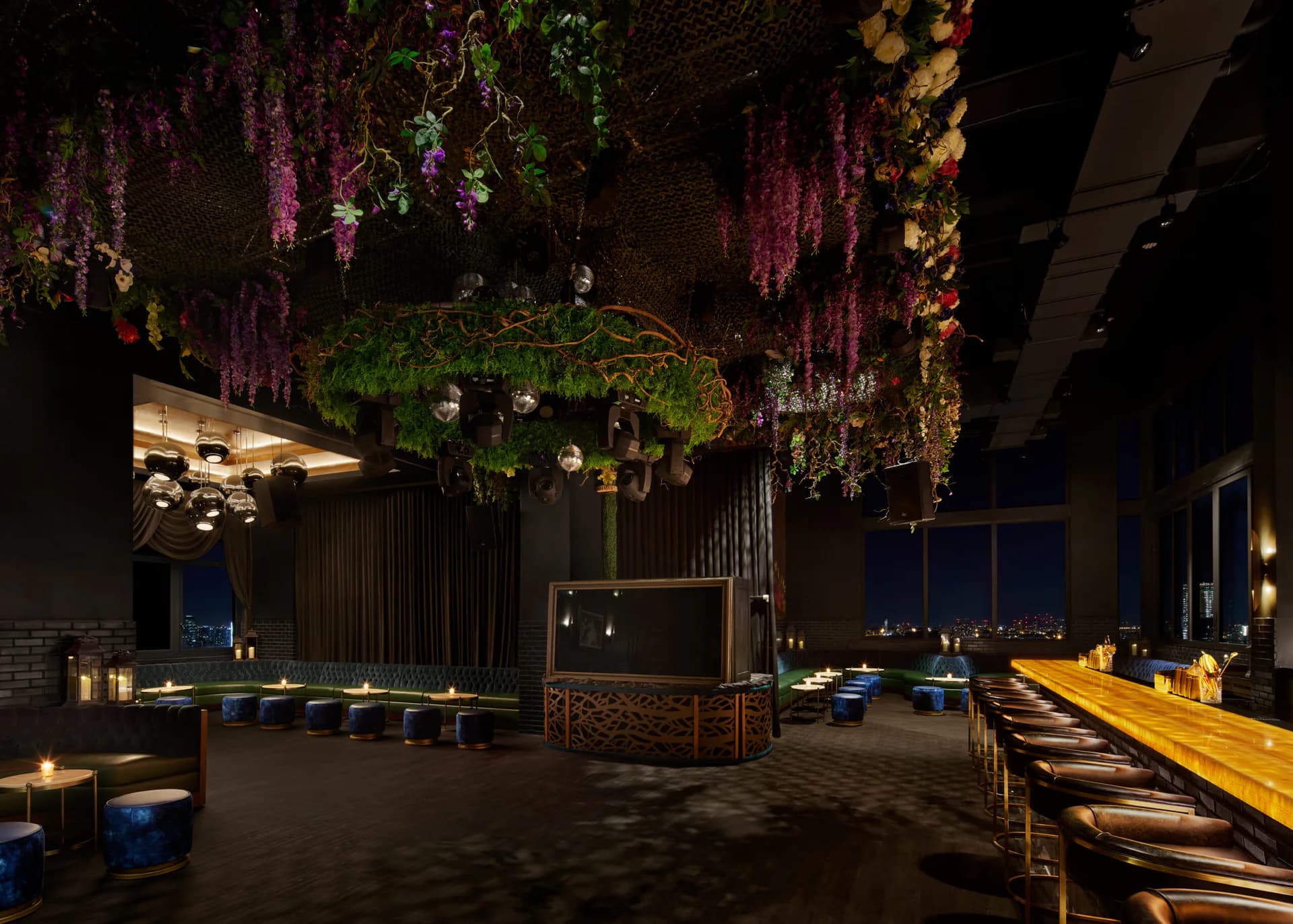 Luxurious modern event space with hanging floral installations in purple and green, ambient lighting, and wood dining tables by Katie Cole.