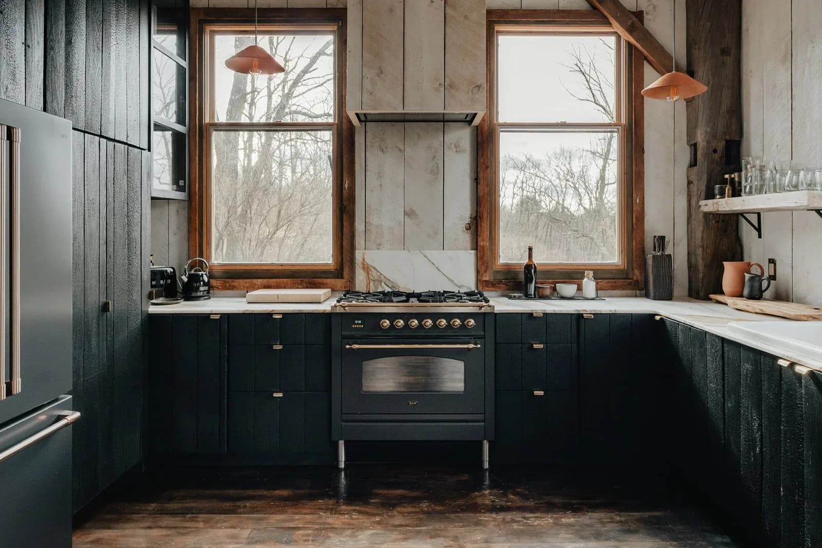 Dark navy kitchen with wooden-framed windows, black range cooker, white countertops, and warm wood flooring by Katie Hartell.
