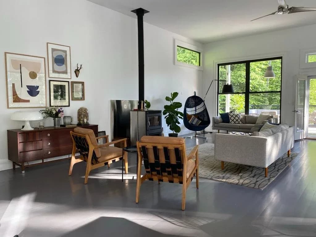 Bright modern living room with wood-burning stove, mid-century wooden chairs, gray sofa, and gallery wall, designed by Katie Hartell.