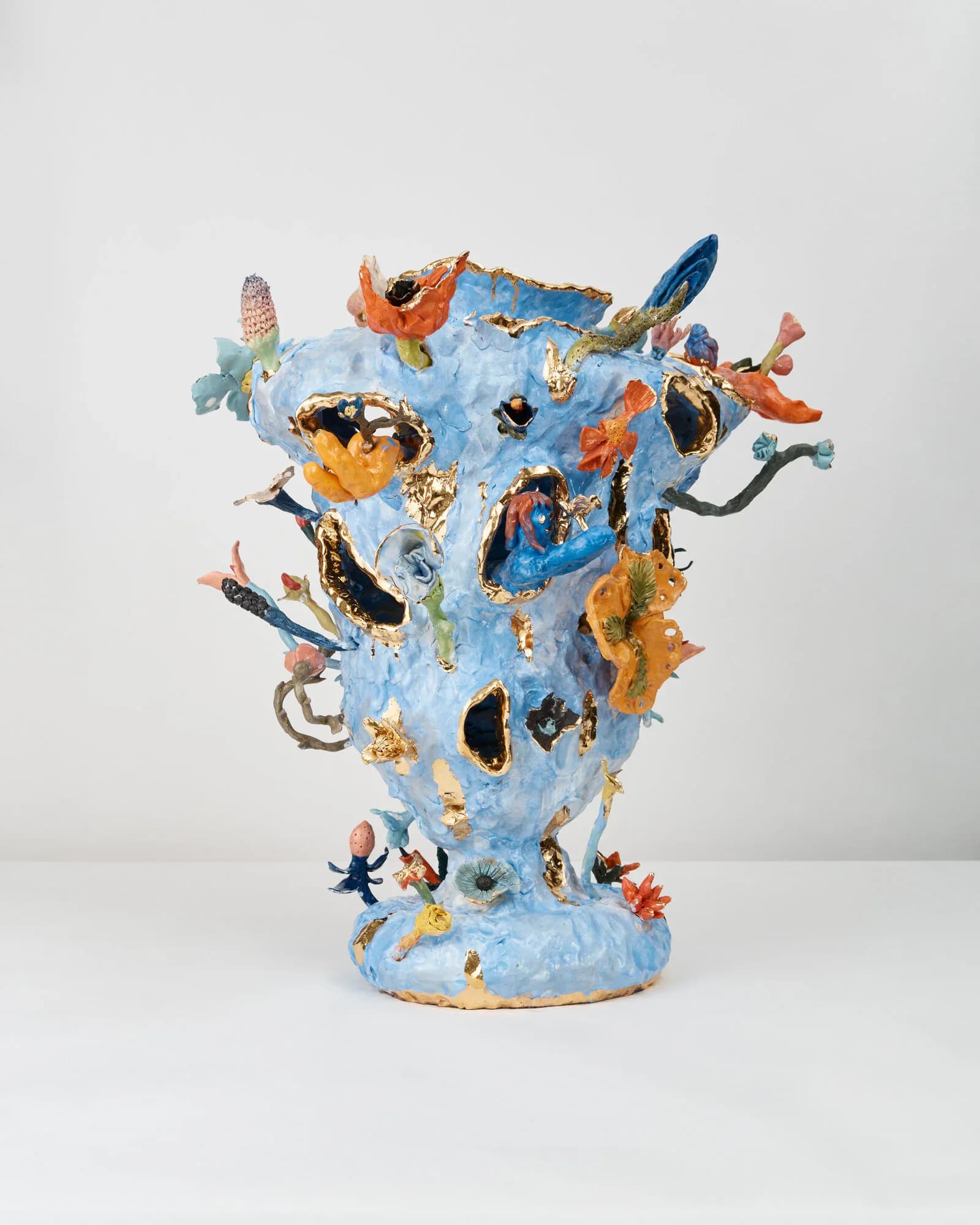 A light blue sculptural vessel densely covered with colorful ceramic and metallic creatures, fish, and abstract forms by Katie Stout.