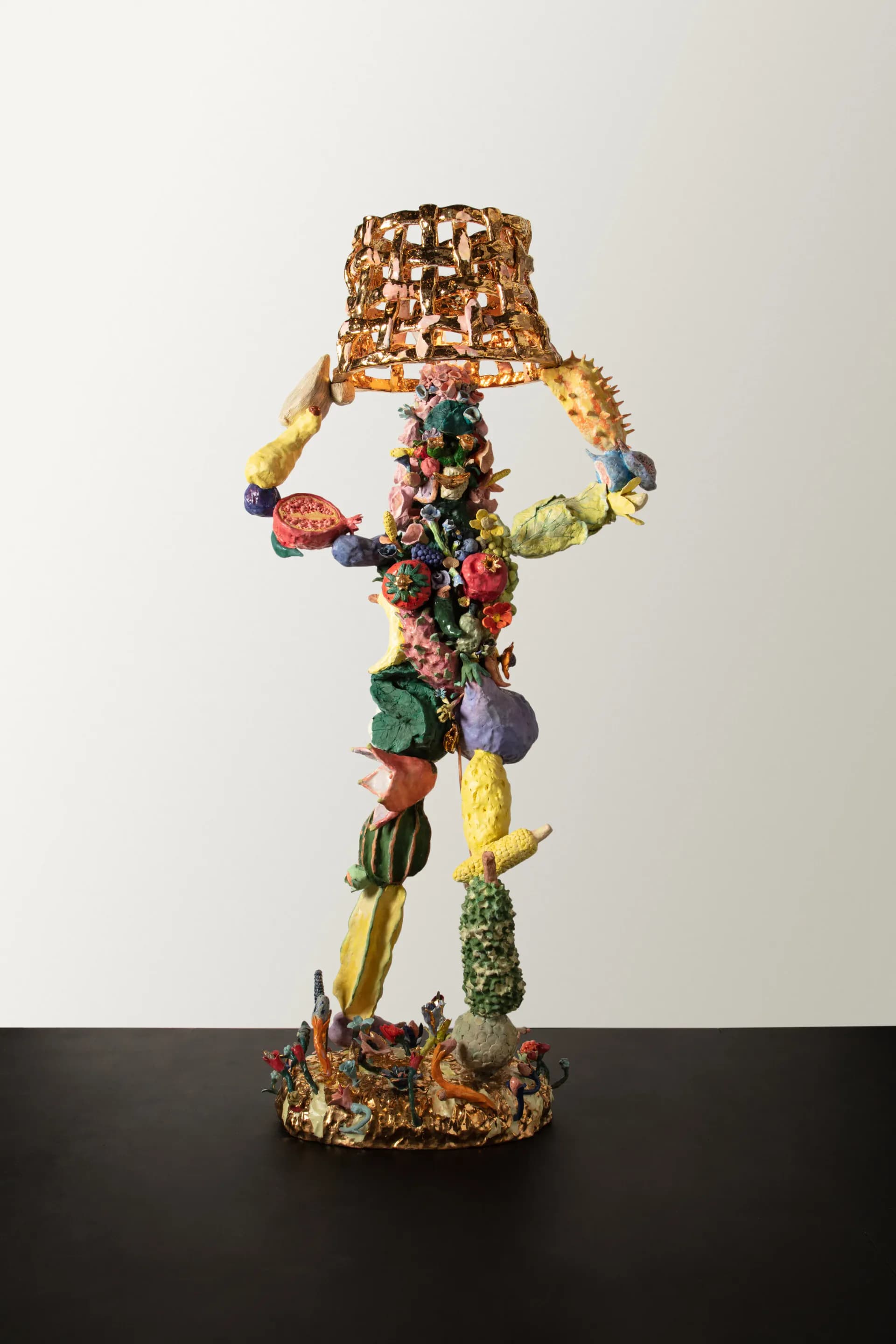 Colorful sculptural installation featuring stacked vegetables, fruits, and fibers arranged in an anthropomorphic form with woven copper crown, by Katie Stout.