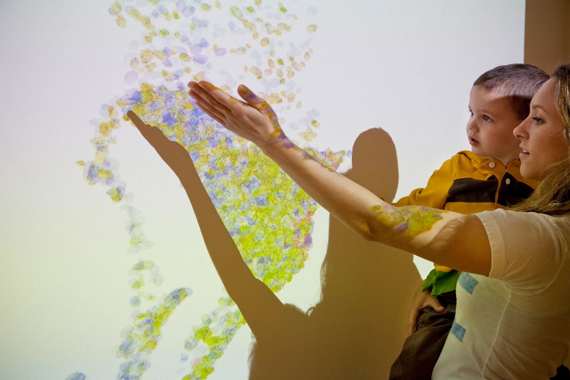 Interactive digital installation with colorful particle projection responding to hand gestures, designed by Kaylie Siwy.