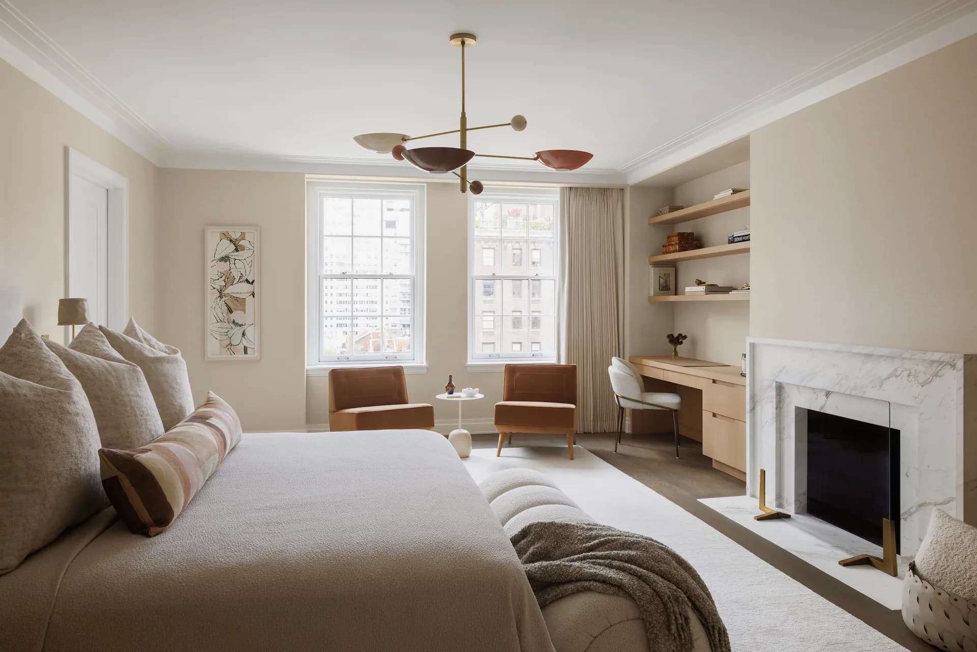 Serene master bedroom with neutral palette featuring a marble fireplace, built-in shelving, mid-century modern furnishings, and large windows by Kelly Aaron.