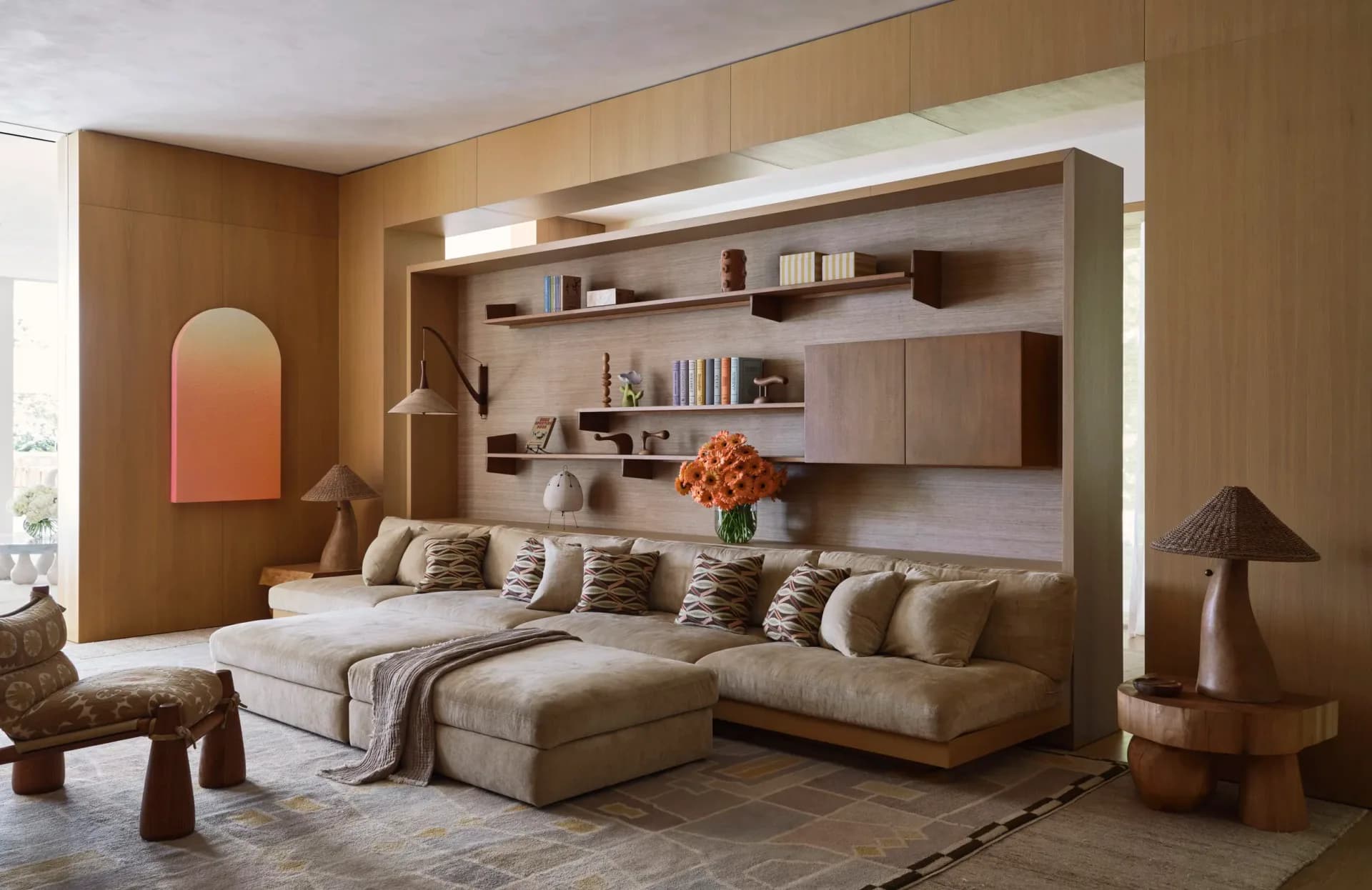Warm-toned living room with built-in shelving, cream sectional sofa, and sculptural wooden furniture by Kelly Behun.