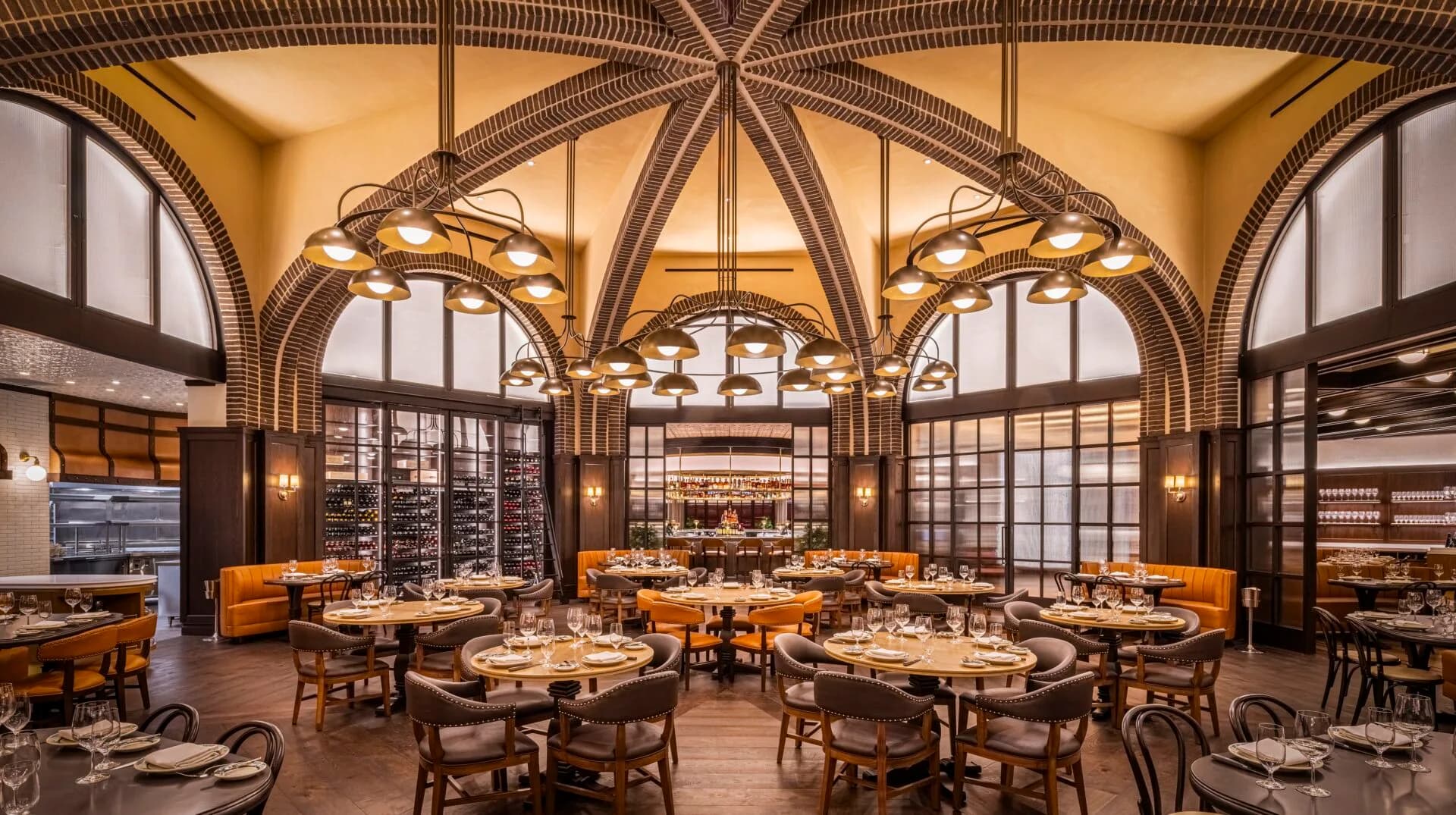 Elegant dining room with soaring barrel-vaulted ceilings, arched windows, warm wood tones, and multiple round tables set for service by Kelsey Verillo.