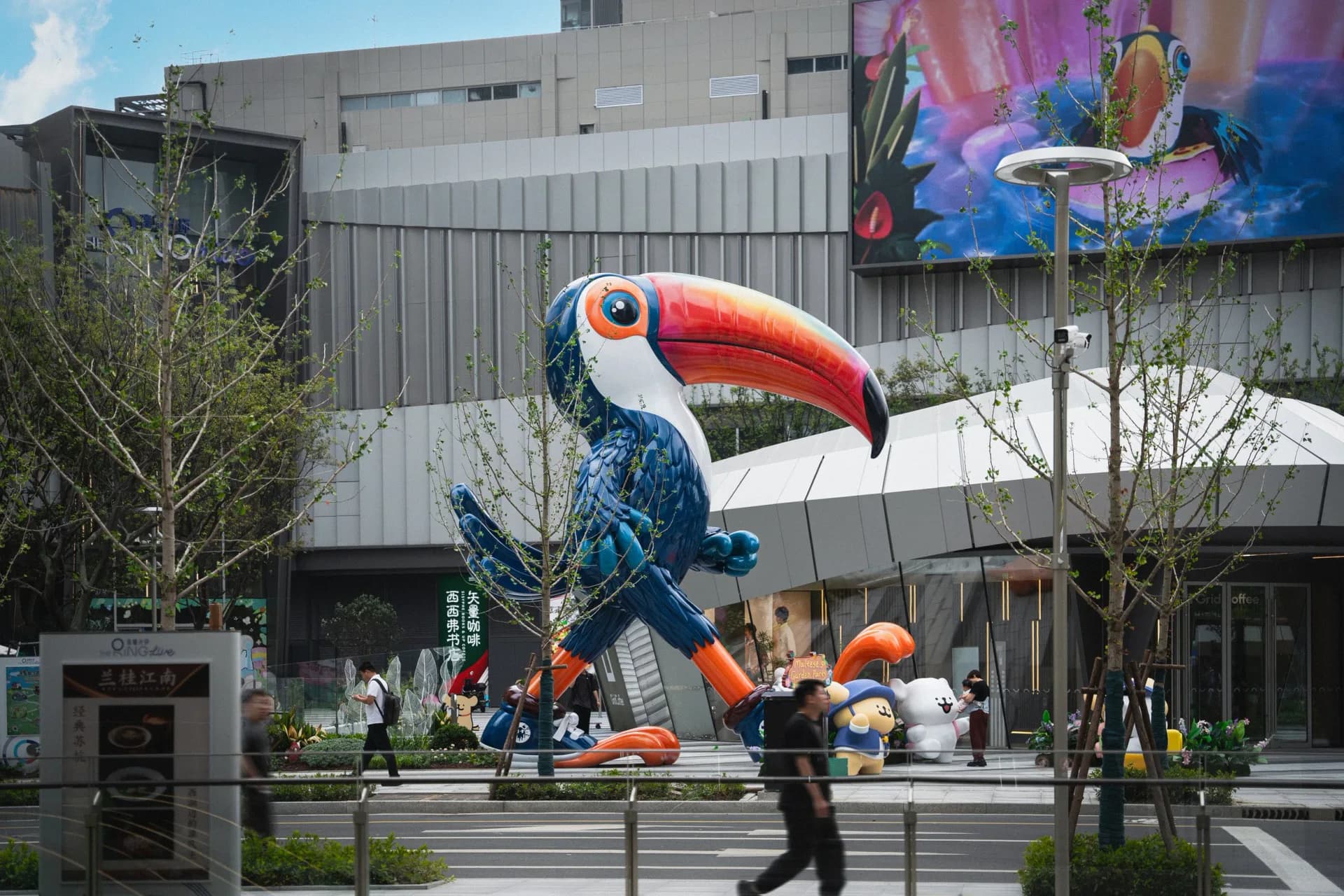 Large-scale public art installation of a colorful toucan sculpture in an urban plaza with modern building backdrop, by Ken Kelleher.