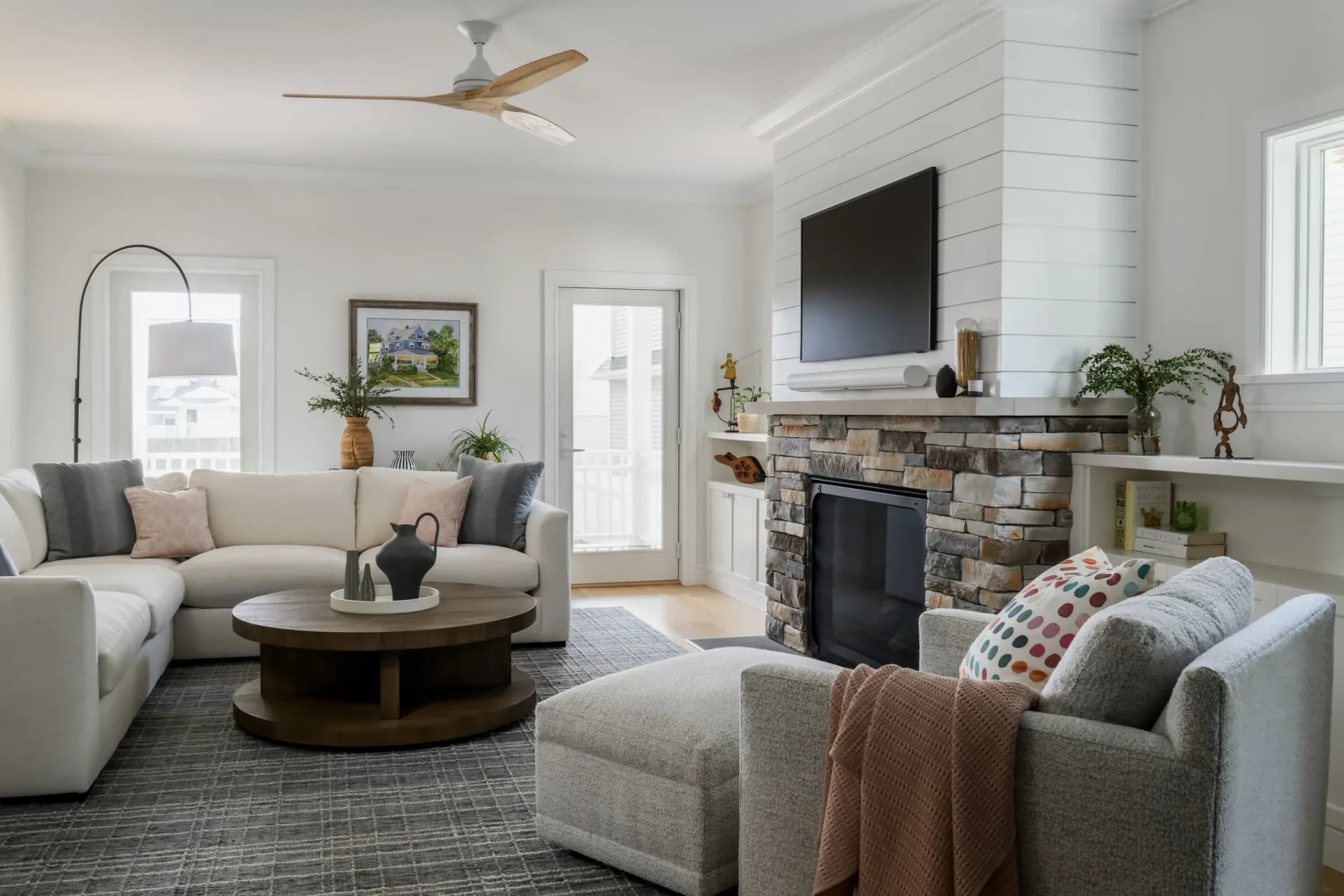 Modern living room with curved cream sectional, round wood coffee table, and fireplace with white shiplap surround and mounted TV by Keri Tickle.