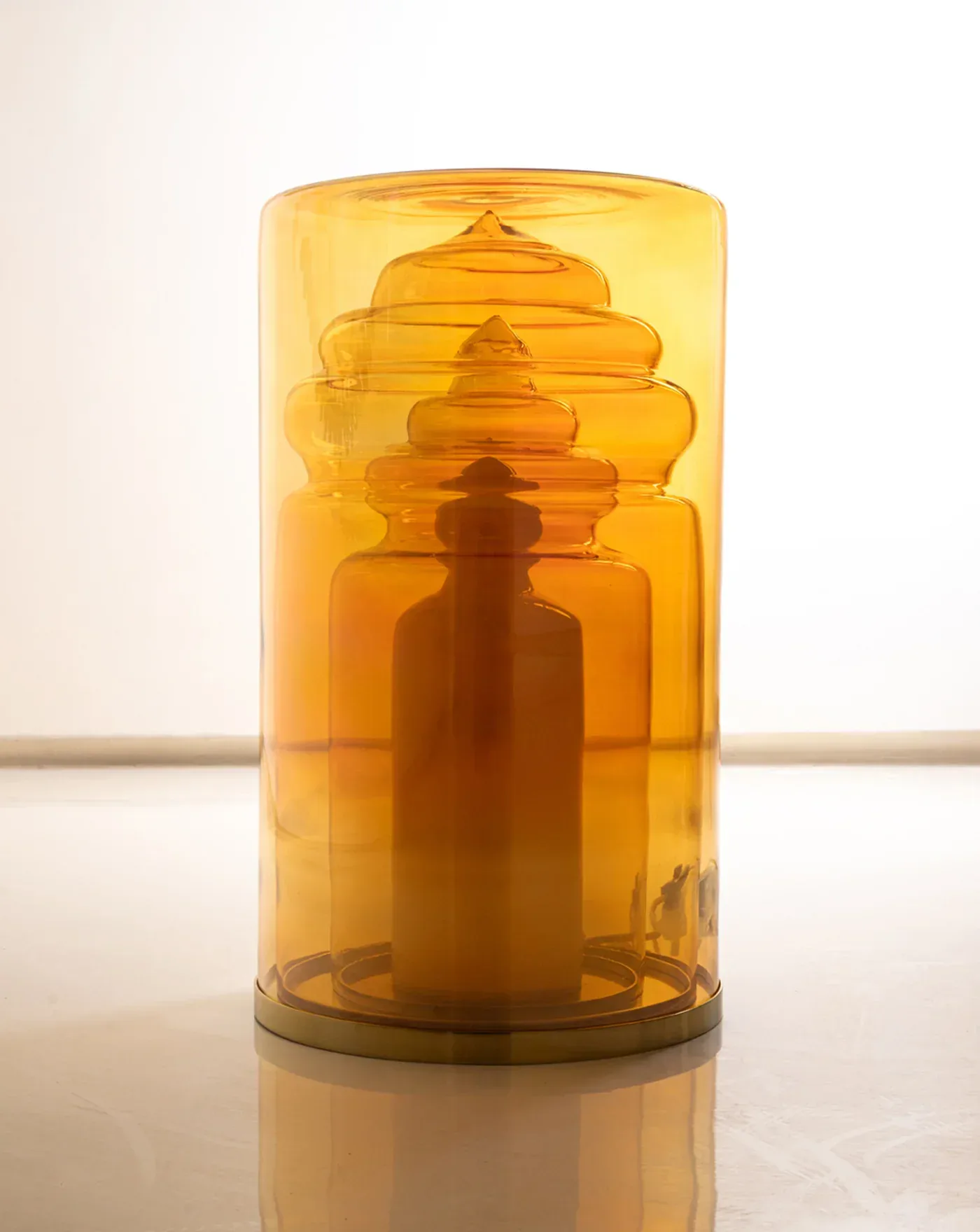 Amber glass cylindrical light fixture with nested dome shapes creating a lighthouse-like silhouette, displayed against a neutral background by Kickie Chudikova.