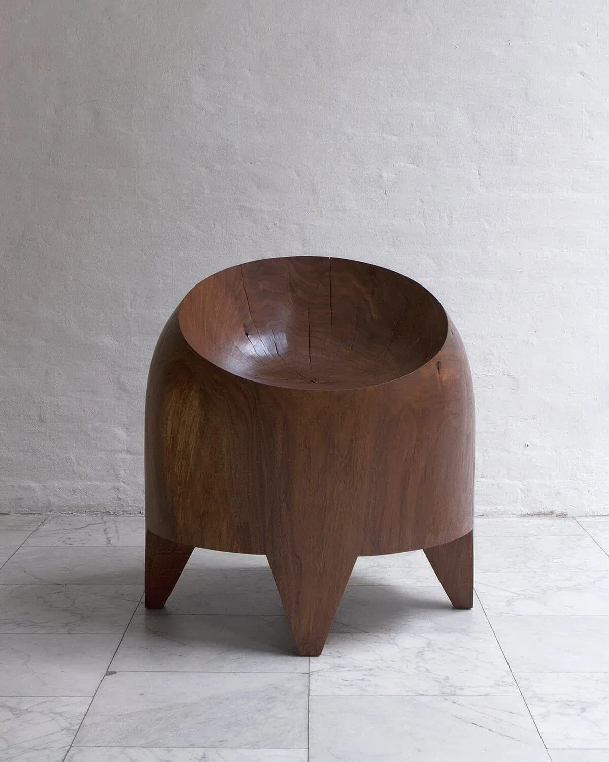 Dark wood sculptural side table with rounded bowl-like top and tapered legs on white floor by Kieran Kinsella.