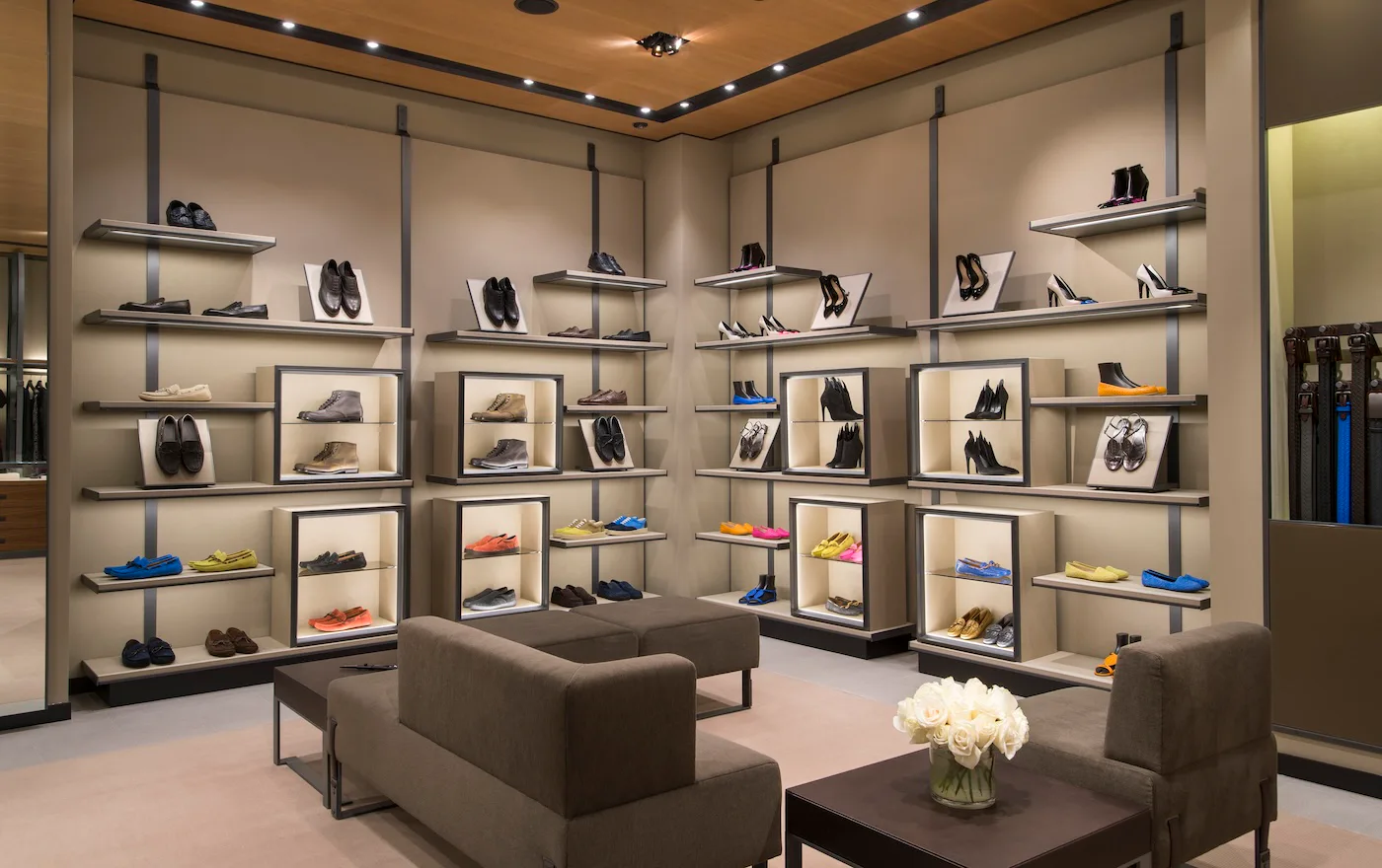 Luxury shoe retail showroom with floor-to-ceiling shelving, neutral palette, gray seating, and sophisticated lighting by EunHea Kim.