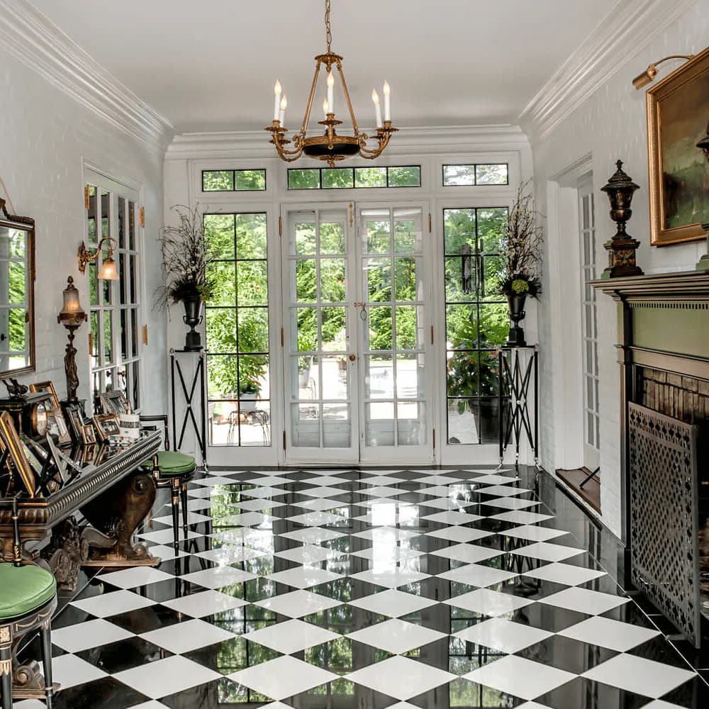 Elegant foyer with black-and-white diamond marble flooring, tall glass French doors, brass chandelier, and classical architectural details by Kim Radovich.