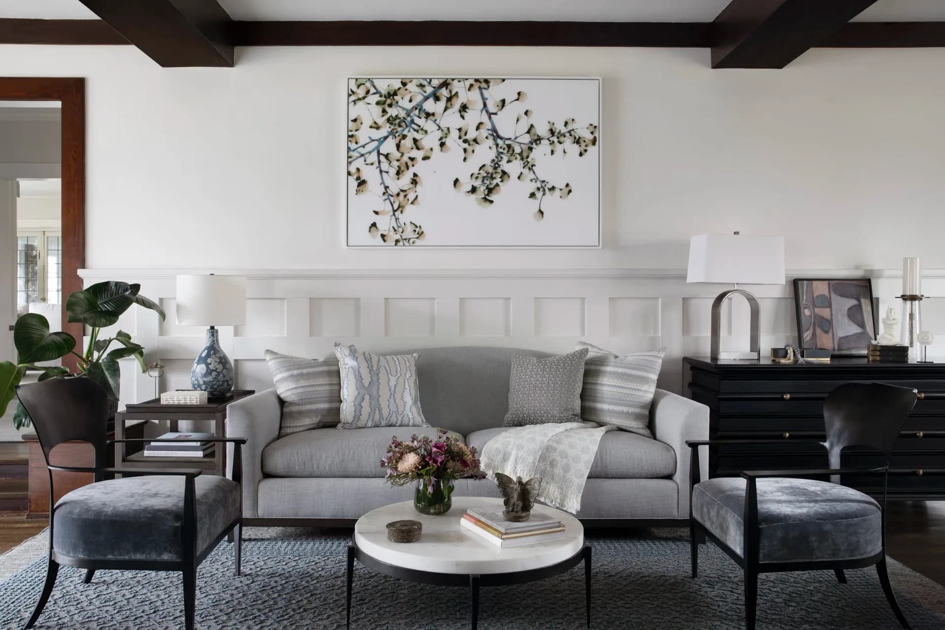 Modern living room with gray sofa, white shiplap fireplace, black nightstands, and blue upholstered ottomans by Kim Mitchell.