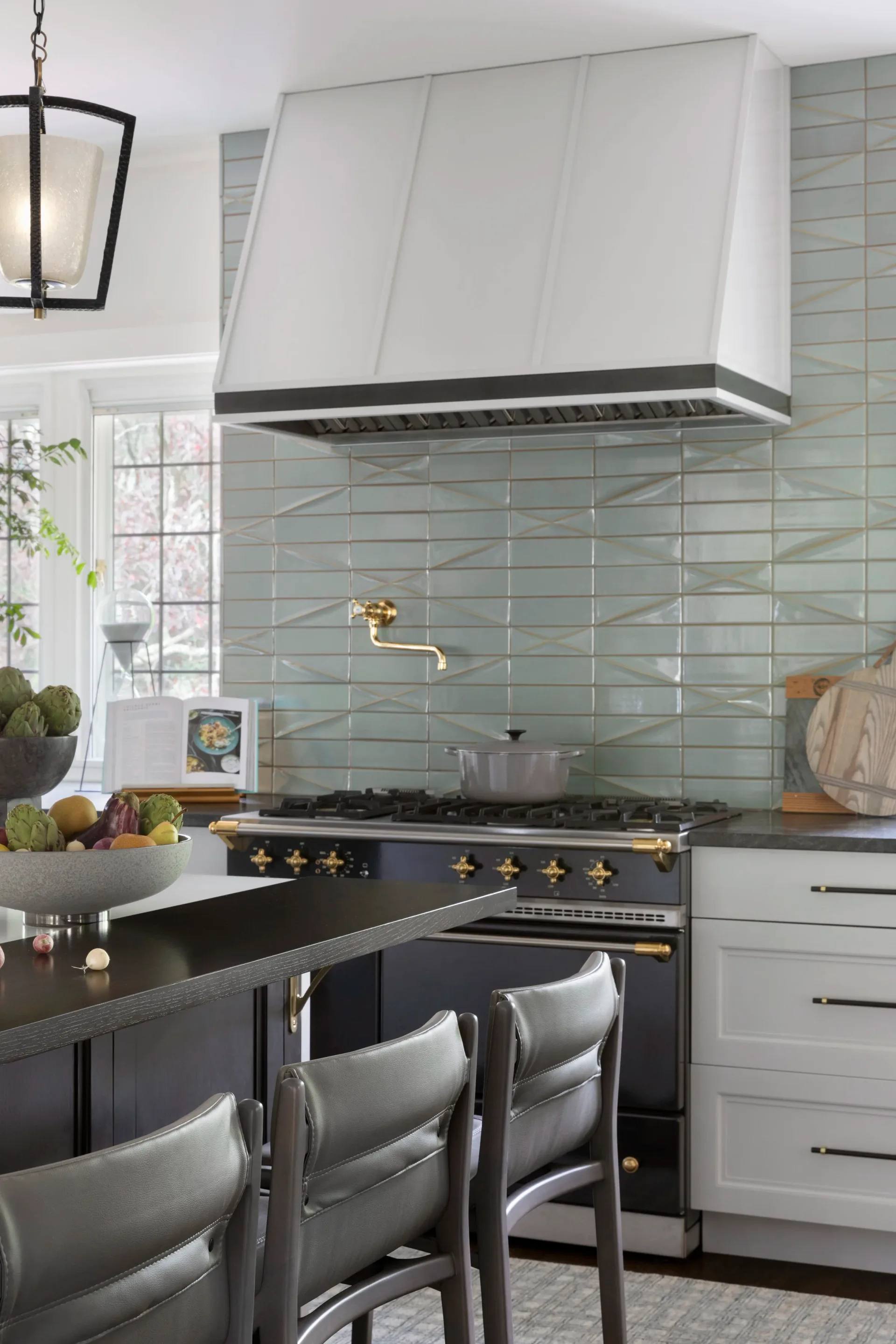 Modern kitchen with white cabinetry, black range with brass accents, sage green subway tile backsplash, and white range hood by Kim Mitchell.