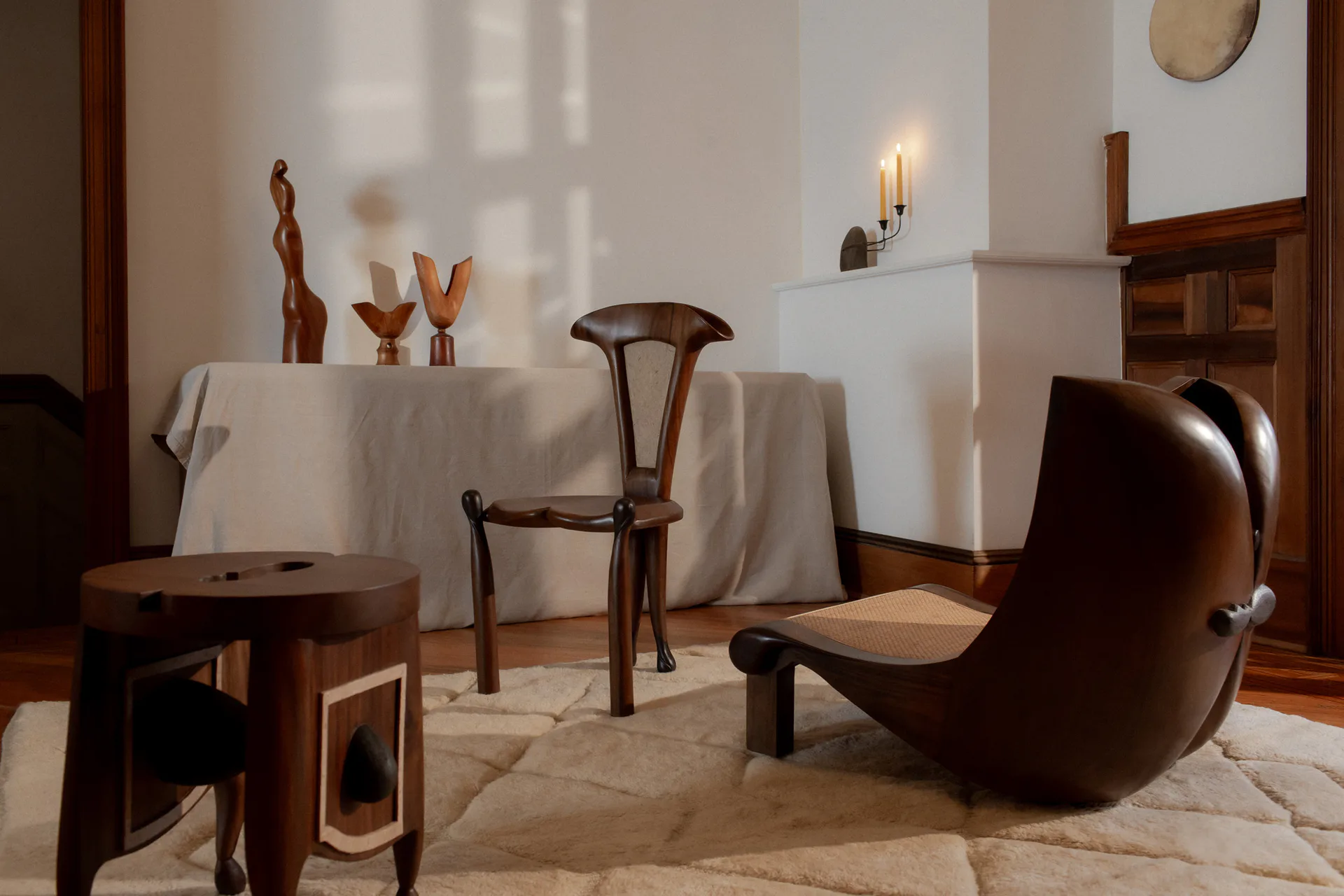 Minimalist interior with warm wood furniture, white draped table, sculptural brown leather chair, and soft natural lighting by Kim Mupangilai.