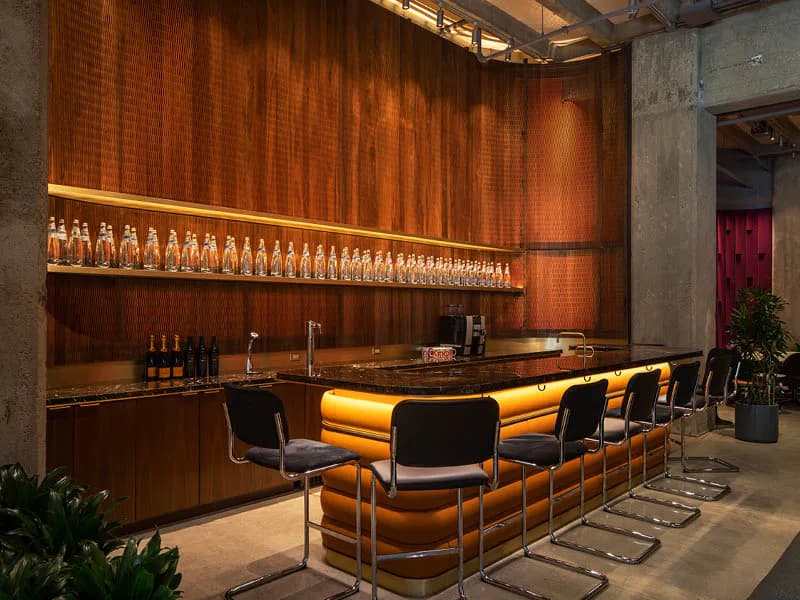 Modern bar interior with warm wood paneling, integrated lighting, and curved orange upholstered seating by Kim Yao.