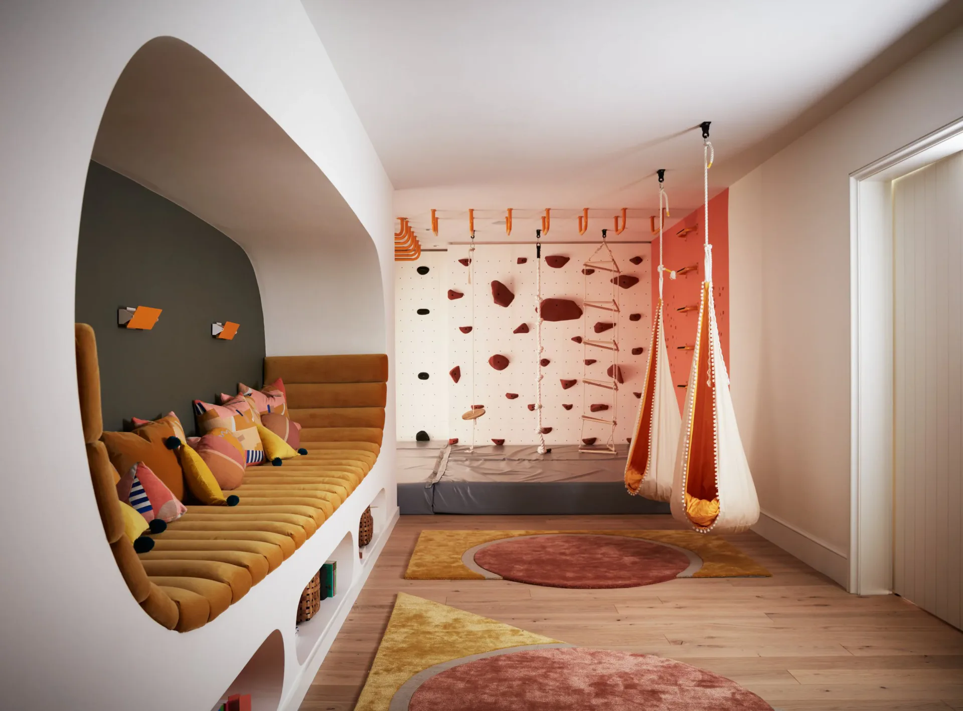 A children's playroom with curved built-in seating nook, climbing wall, rope features, and geometric patterned rug in warm orange and wood tones, designed by Kirsten Flanigan.