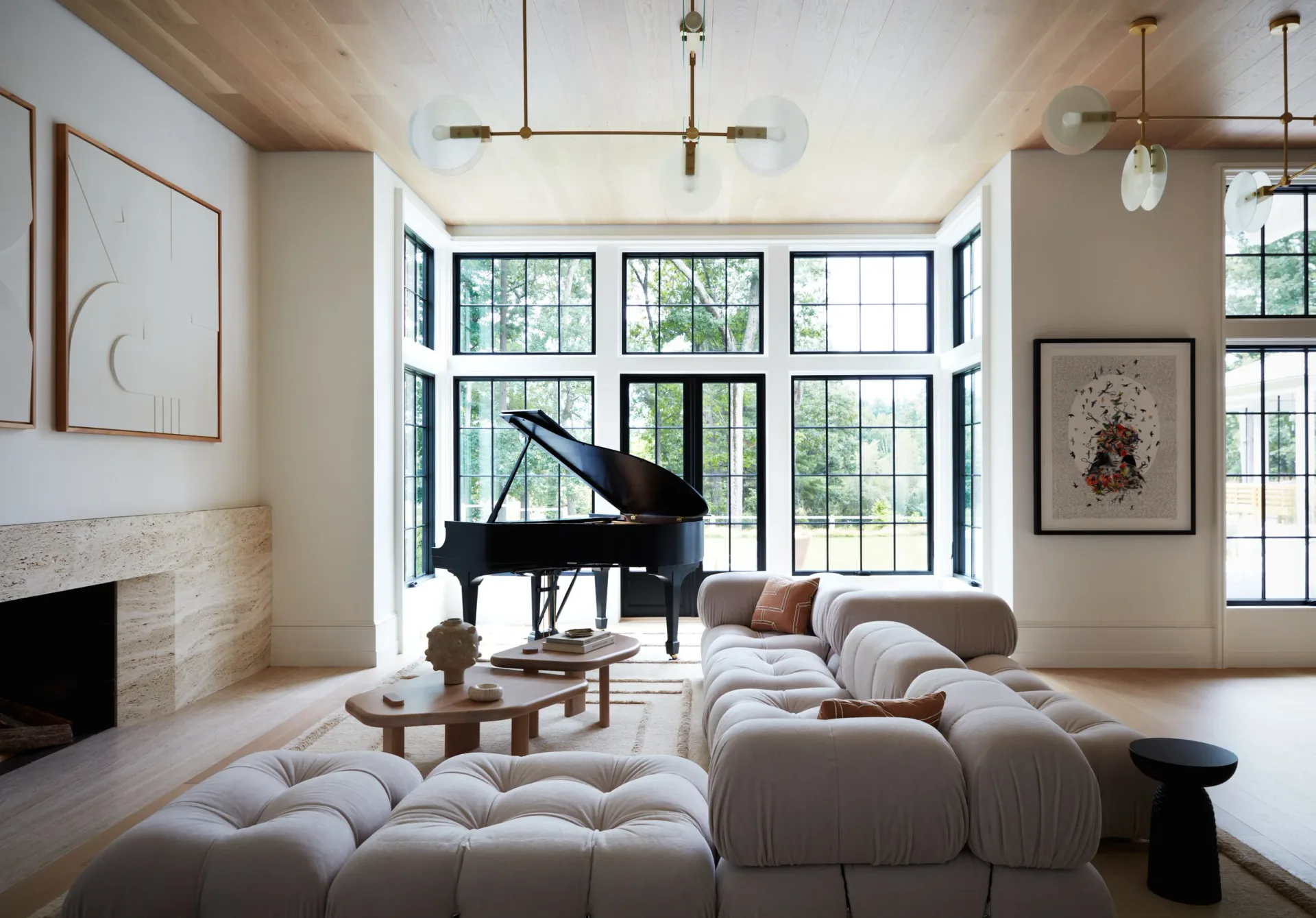 Bright modern living room with grand piano, sculptural cream seating, fireplace, and expansive grid windows by Kirsten Flanigan.
