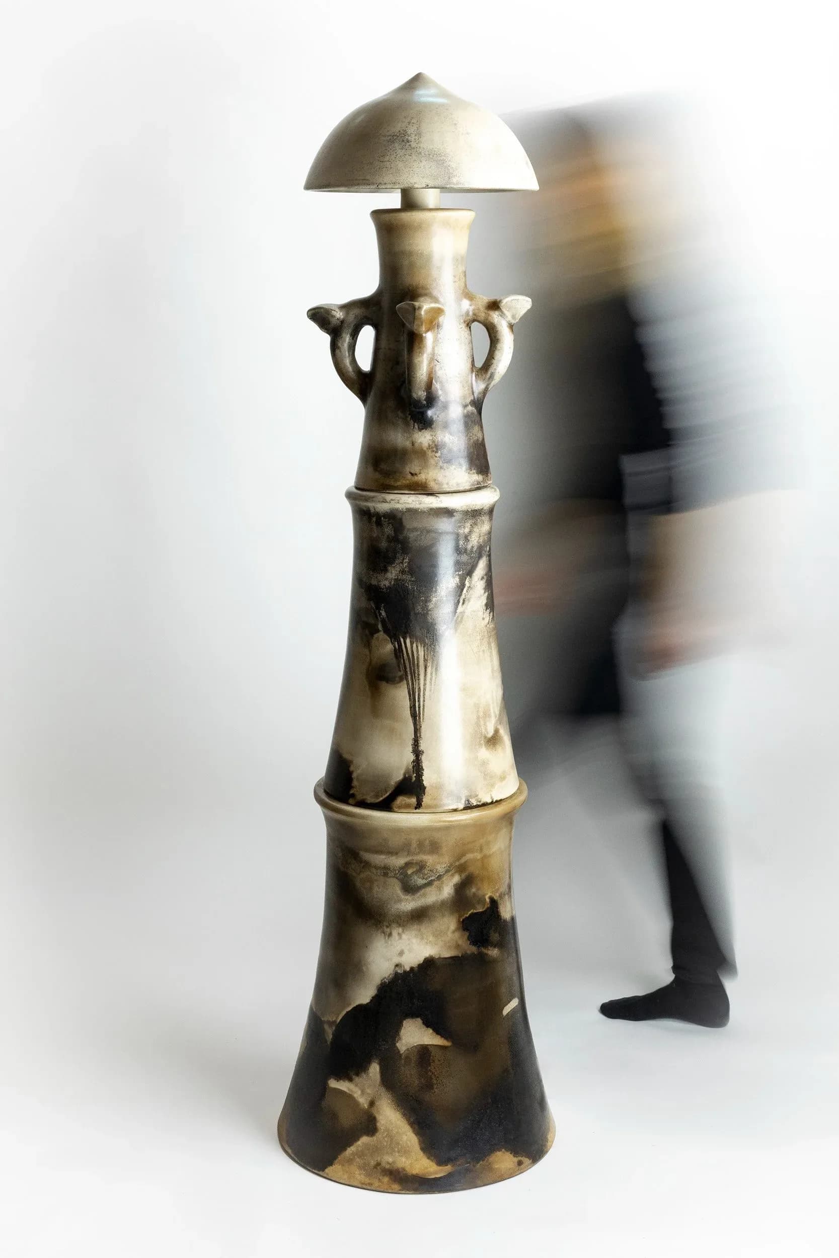 Tall brass sculptural vessel with dome top and handles, showing patina and organic form, displayed in gallery space by Kristin Victoria Barron.