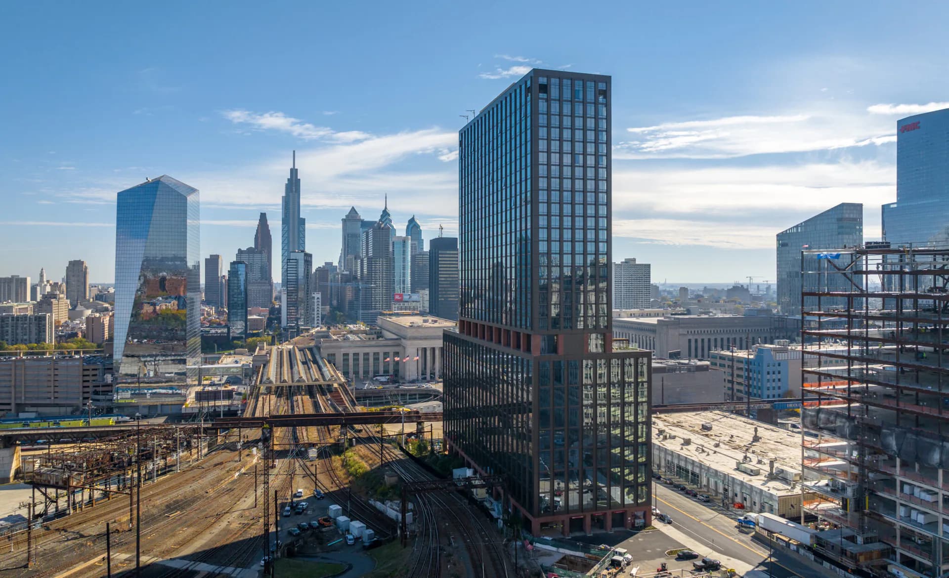 Aerial view of a modern Manhattan street corner with tall residential and commercial buildings, railroad yards, and clear city skyline, showcasing urban architectural development by Kutay Biberoglu.