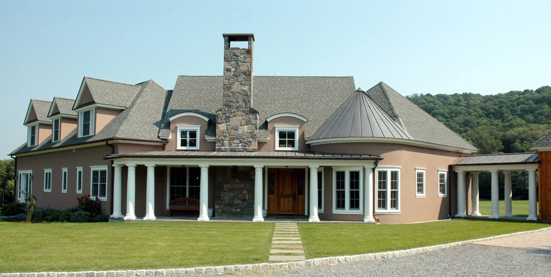 A traditional brick colonial residence with stone chimney, white columns, dormer windows, and manicured lawn, designed by Lainie Gahagan.