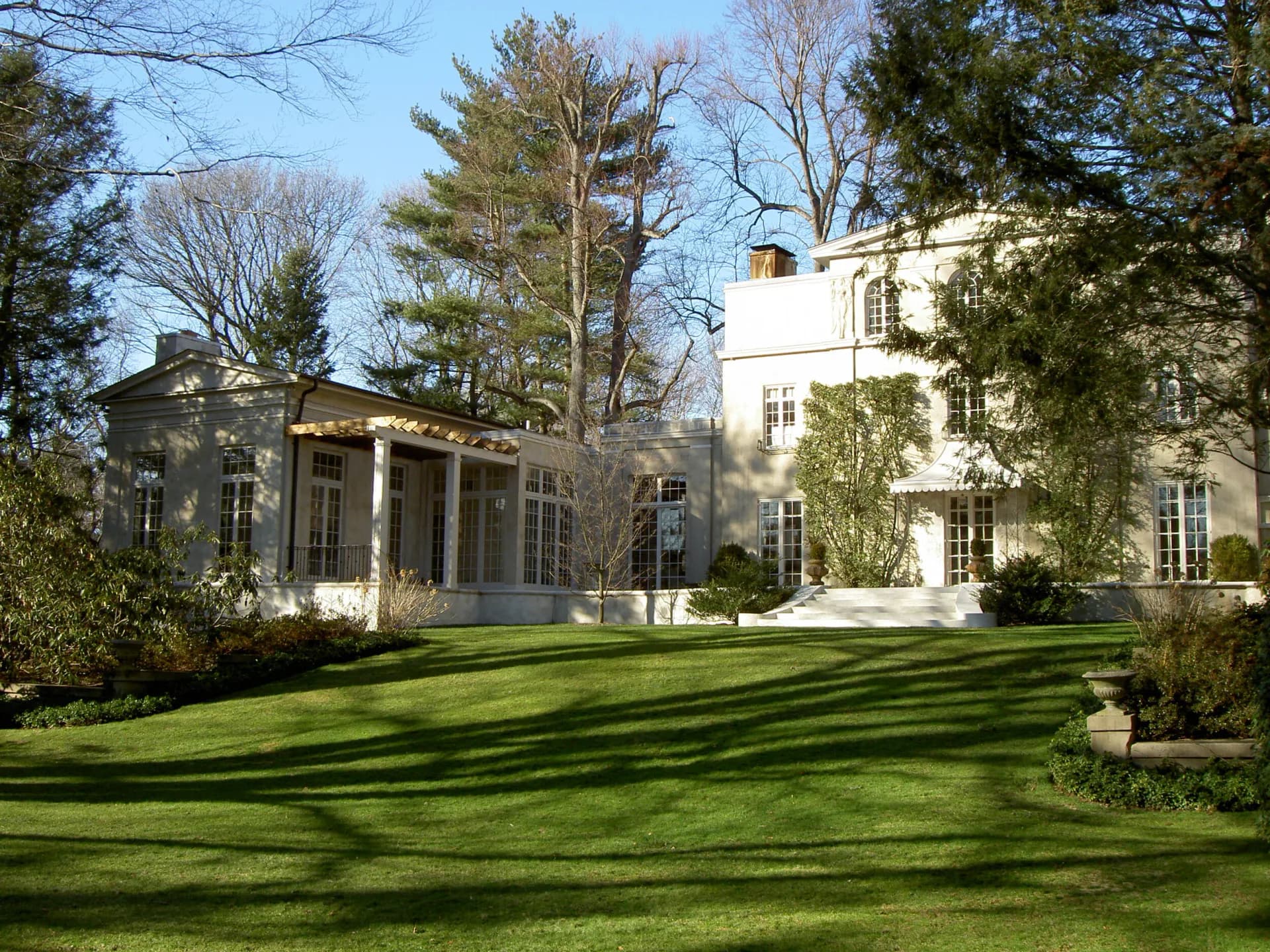 A modernist white residence with columned portico overlooks manicured lawn and mature trees, designed by Lainie Gahagan.