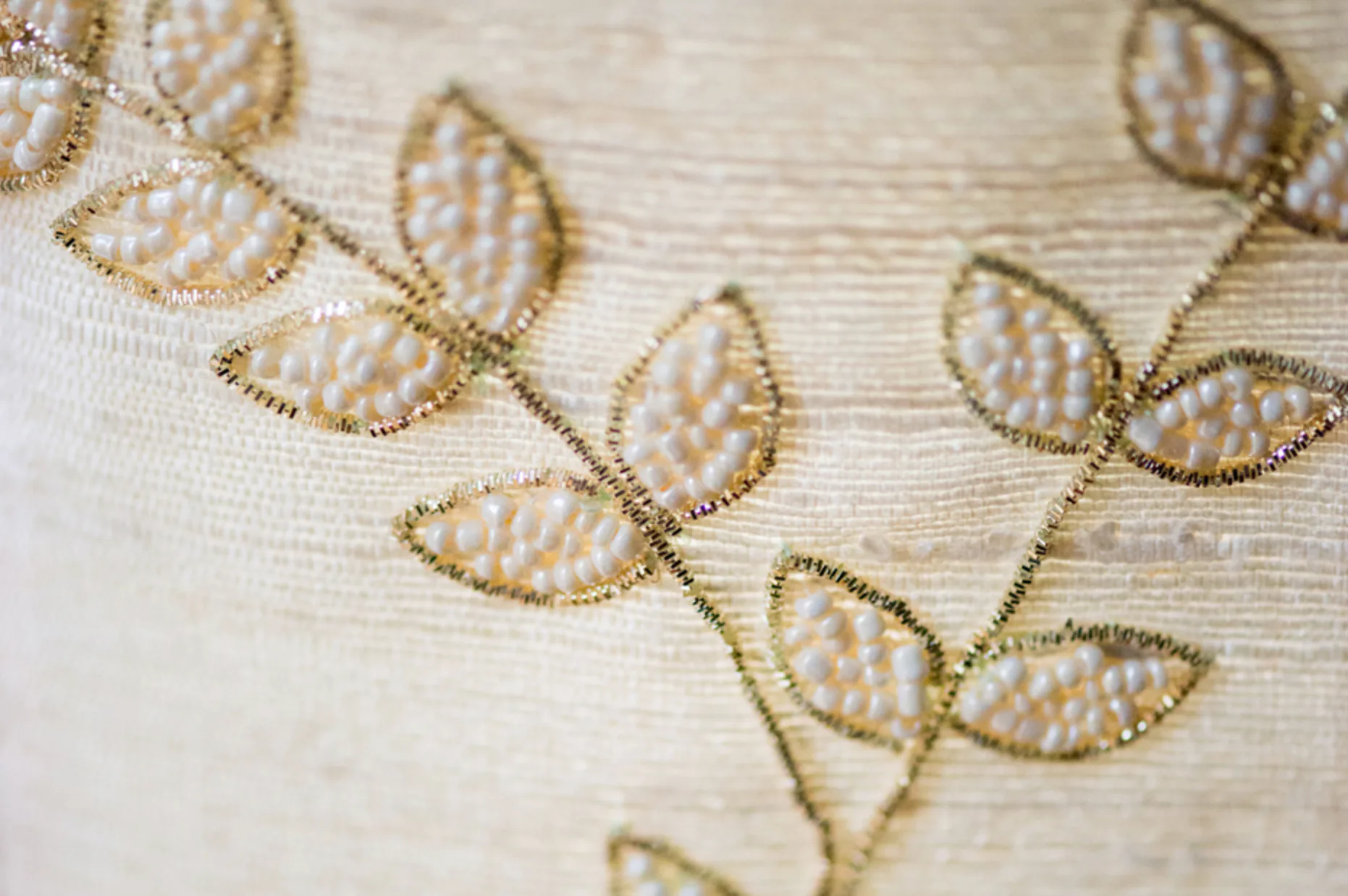 Close-up of delicate gold embroidery with leaf motifs on cream fabric, showcasing detailed textile design work by Lakbir Mahajan.