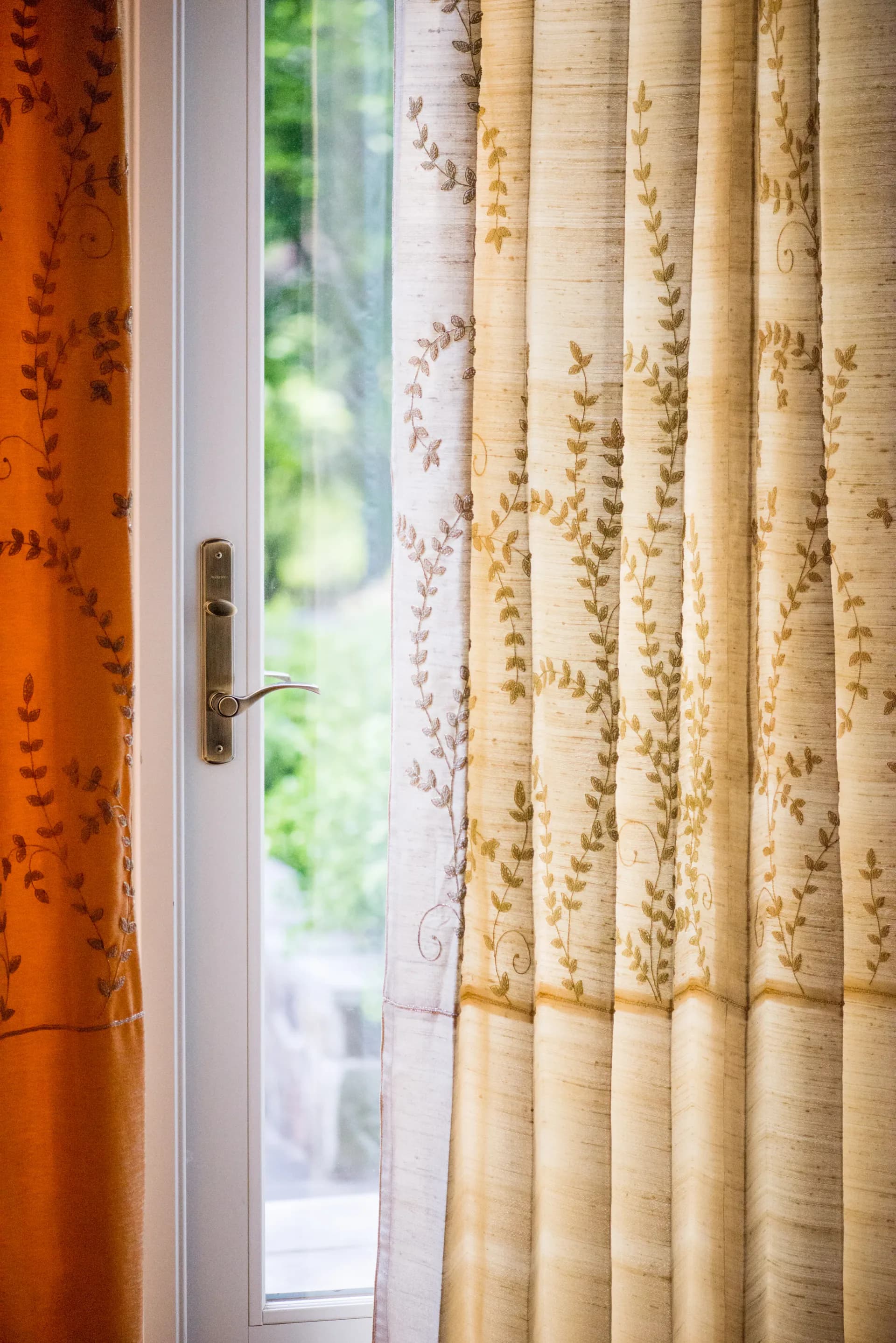 Interior photograph of an open French door with elegant curtains featuring leaf patterns in cream and gold tones, designed by Lakbir Mahajan.