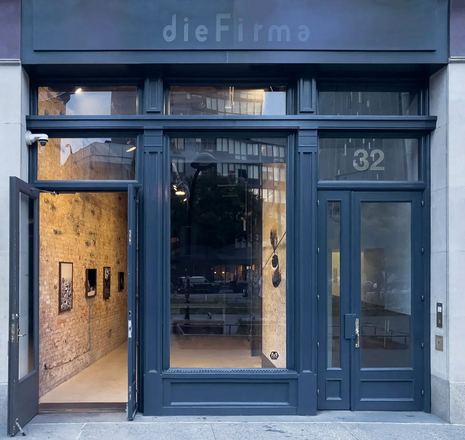Storefront facade with dark blue framing, brick interior wall, and large windows for 'dieFirma' retail space by Laura Blaszczak.