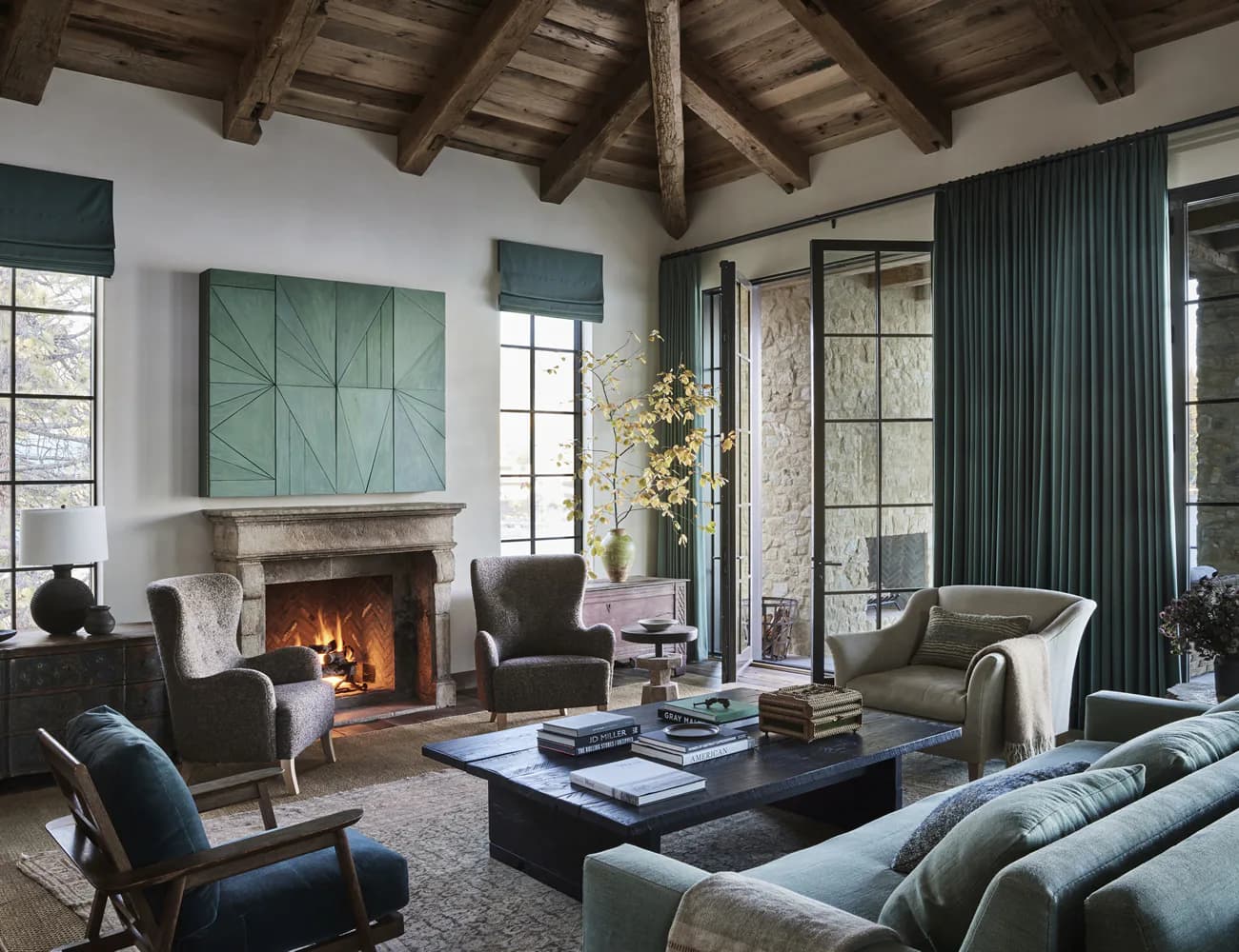 Sophisticated living room with exposed timber ceiling, fireplace, dark leather seating, and floor-to-ceiling curtains designed by Lauren Bensmiller.