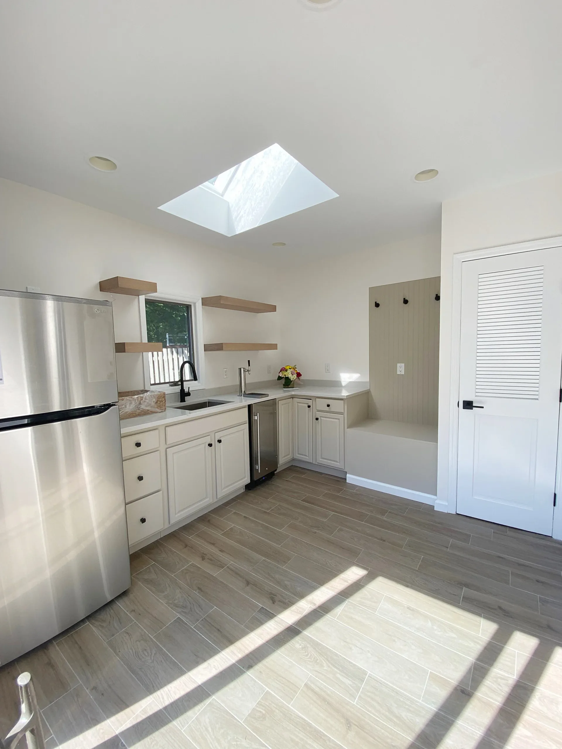 Modern kitchen with white cabinetry, stainless steel appliances, wooden shelving, skylight, and hardwood flooring by Lauren Farhi.