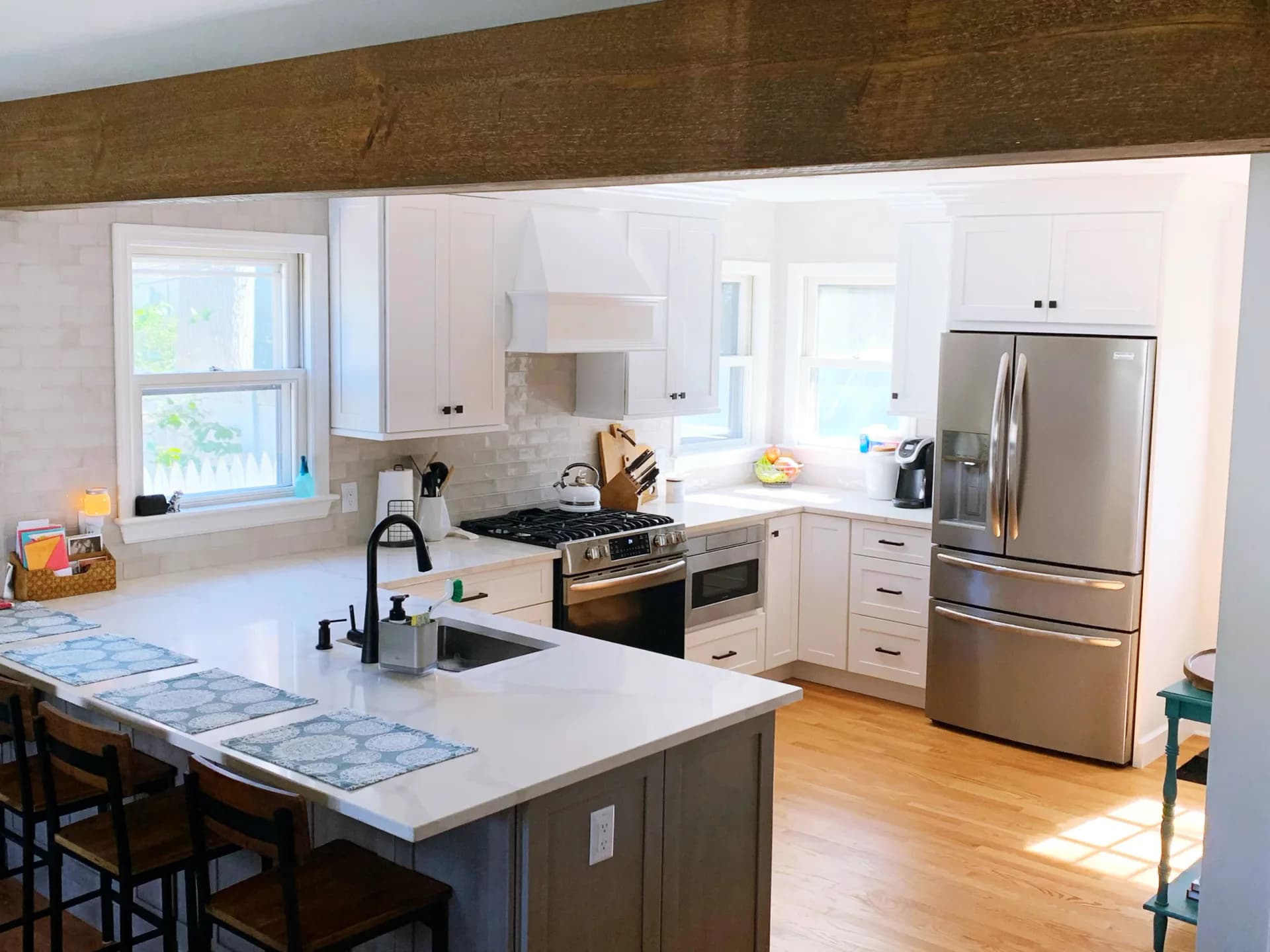 Modern kitchen with white cabinetry, stainless steel appliances, white quartz countertops, gray island, and hardwood floors designed by Lauren Farhi.