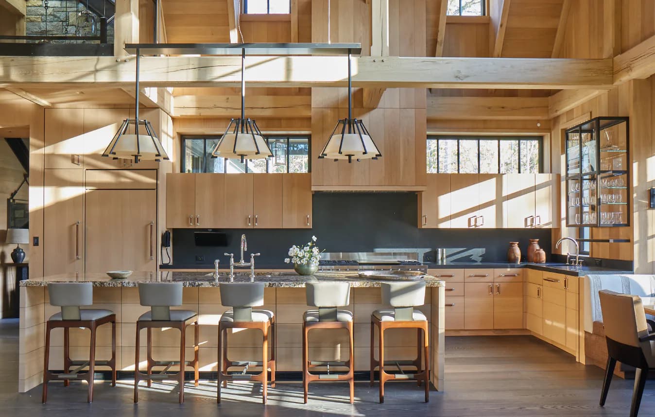 Warm wood kitchen with natural light, dark countertops, island seating, and industrial pendant lighting by Leah Amelung.