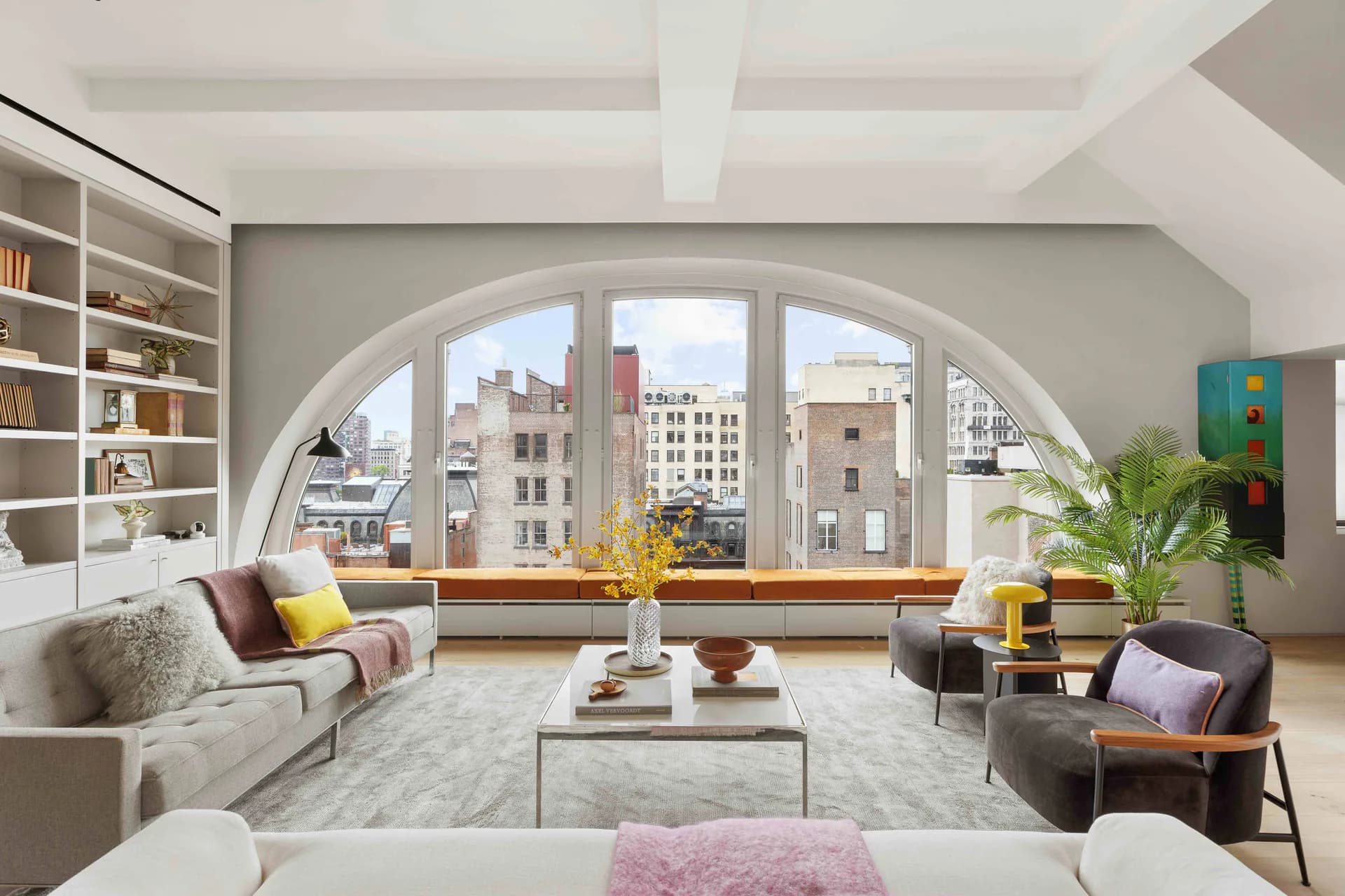 Modern penthouse living room with arched window, city views, neutral palette, and mid-century furniture by Leo Sguera.